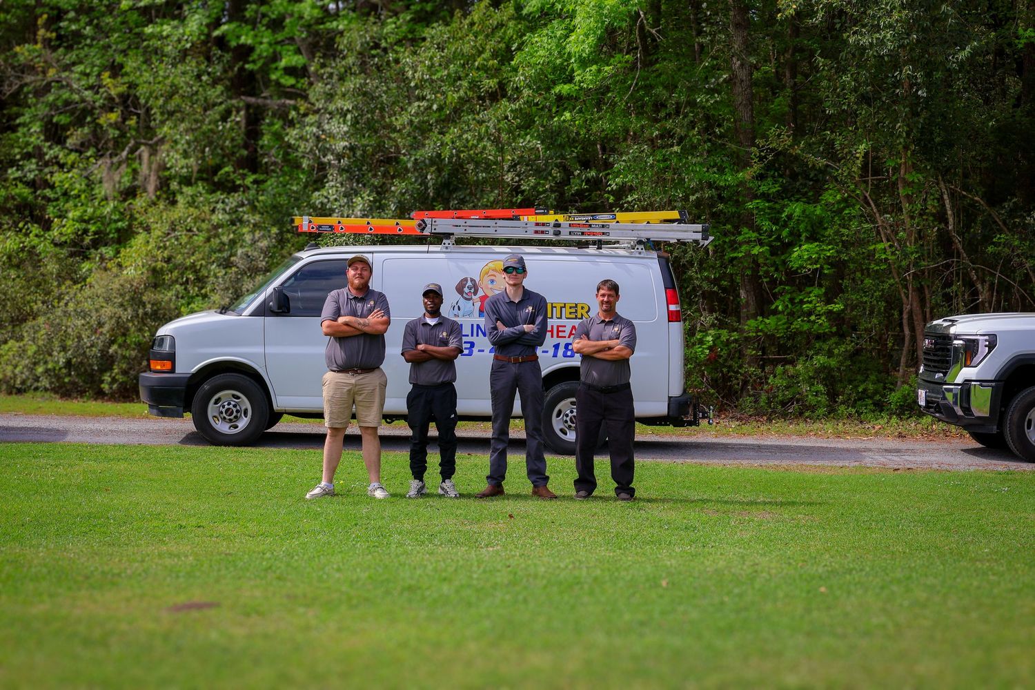 Service vehicles and team members lined up on a grassy area near wooded area.