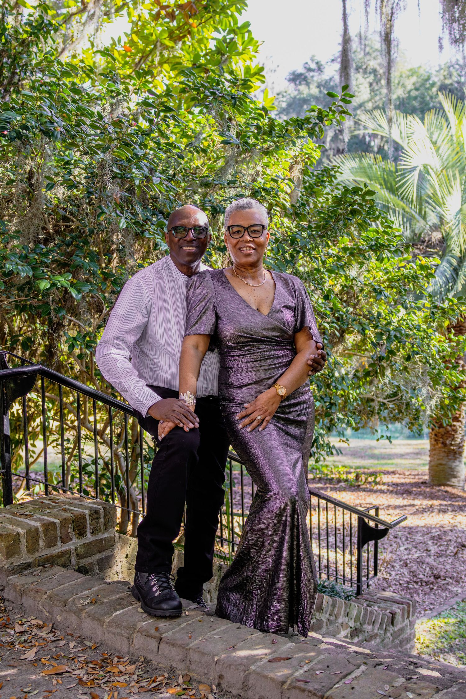 Two people in formal attire posing on stone steps in a garden setting.