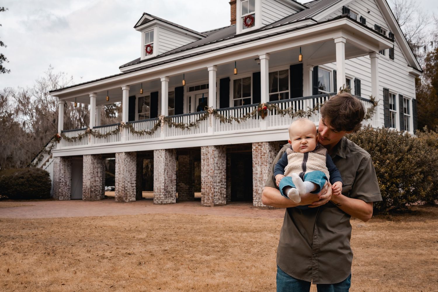 A grand white colonial mansion with tall pillars and wraparound porch stands on a hill.
