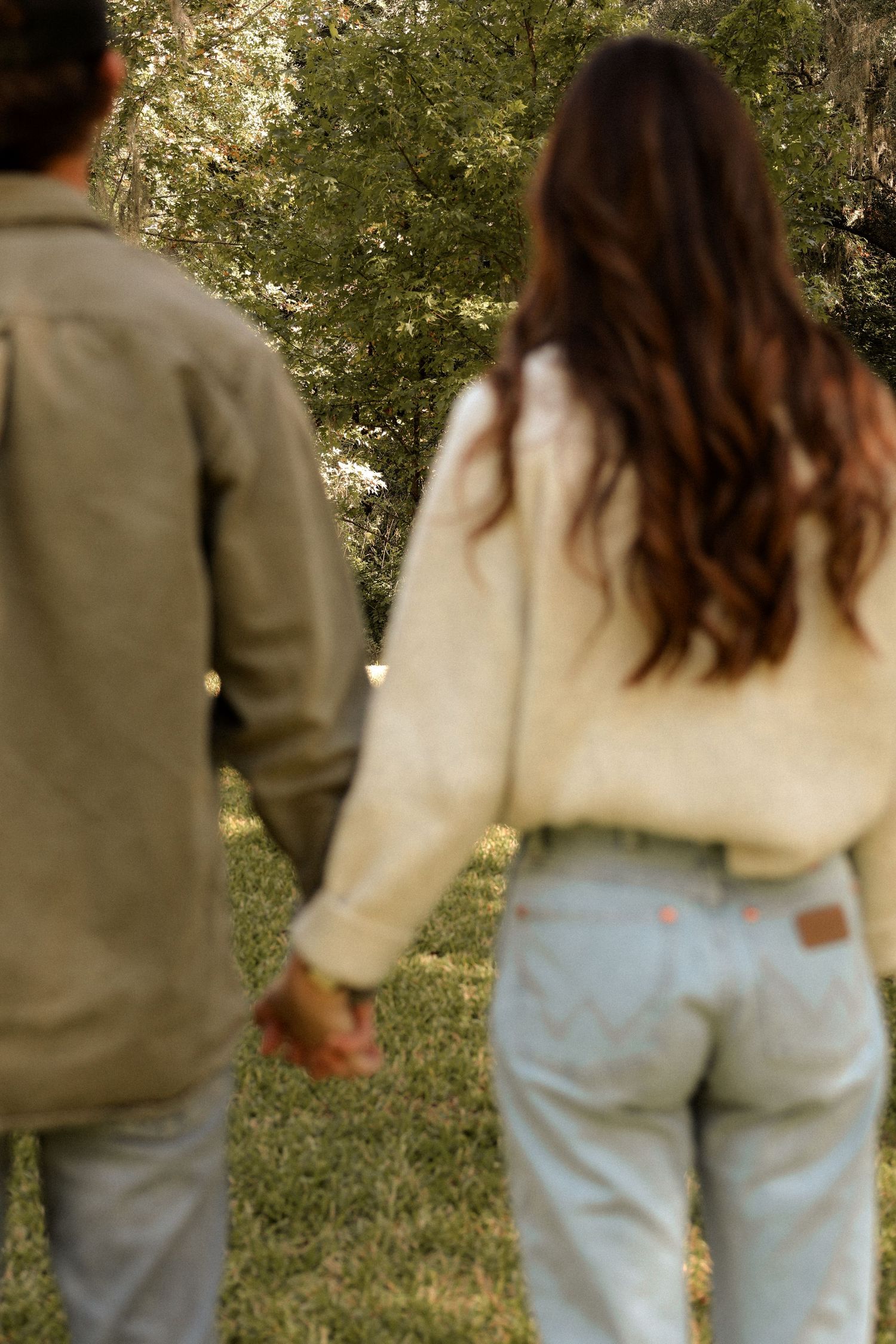 Two people walking hand in hand through a sunlit garden wearing casual attire.
