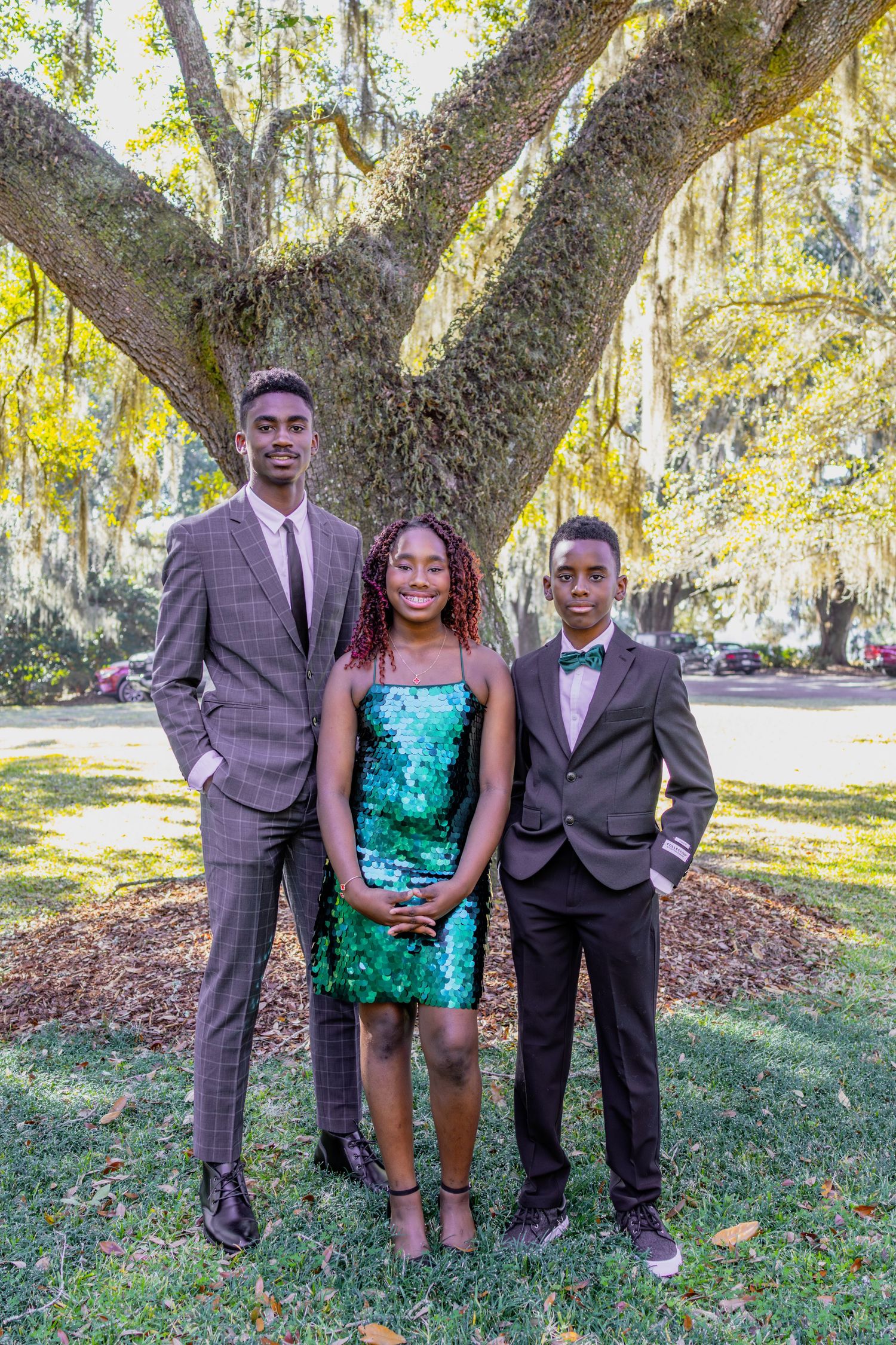 Formal portraits of people in suits and a turquoise dress under oak trees.