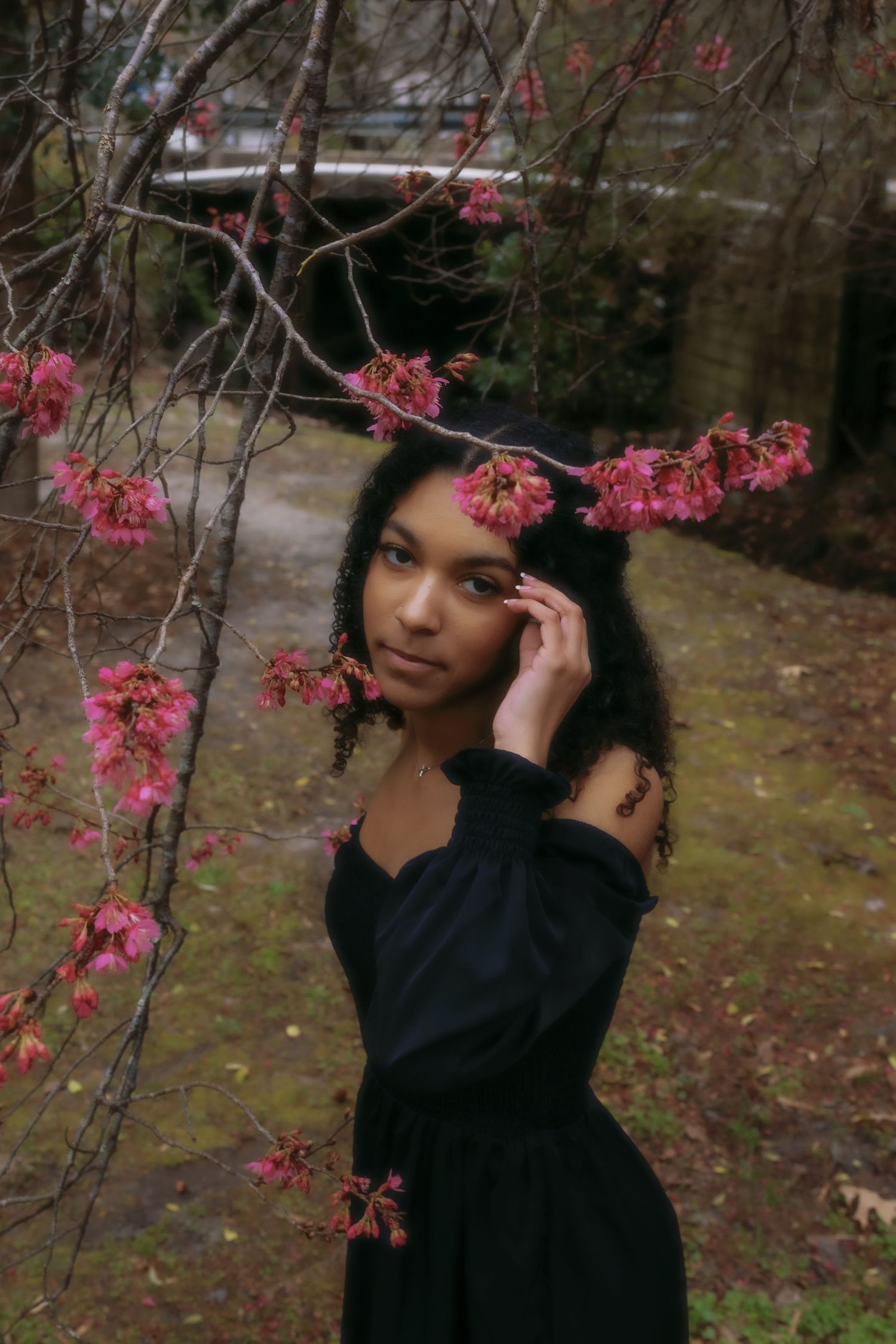 Artistic portrait with pink cherry blossoms framing the composition in a garden setting.