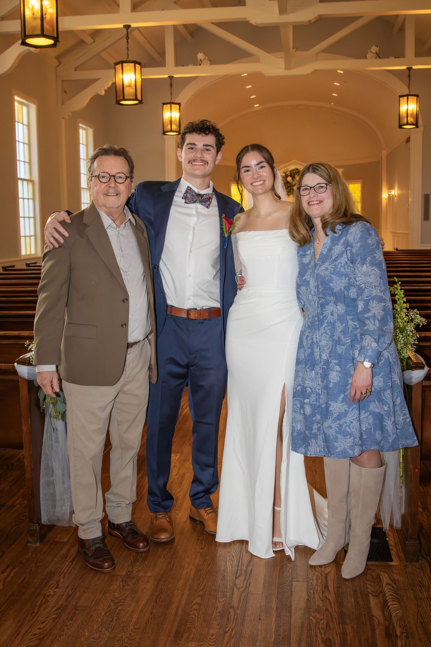 Family group photo in formal attire inside wedding venue with exposed beam ceiling.