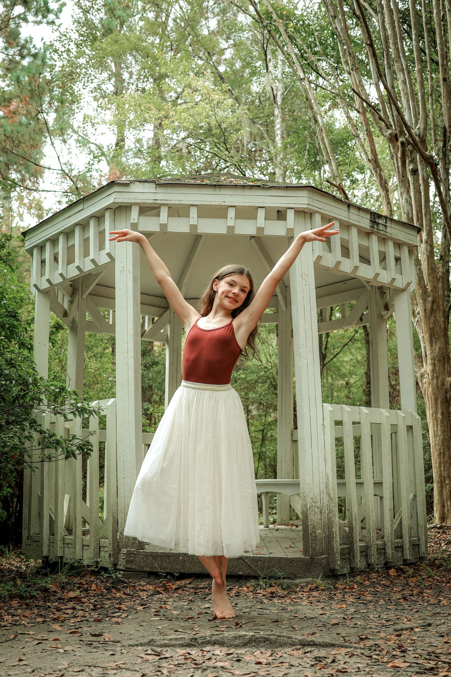 A dancer strikes a jubilant pose in a white tulle skirt and burgundy top under a gazebo.