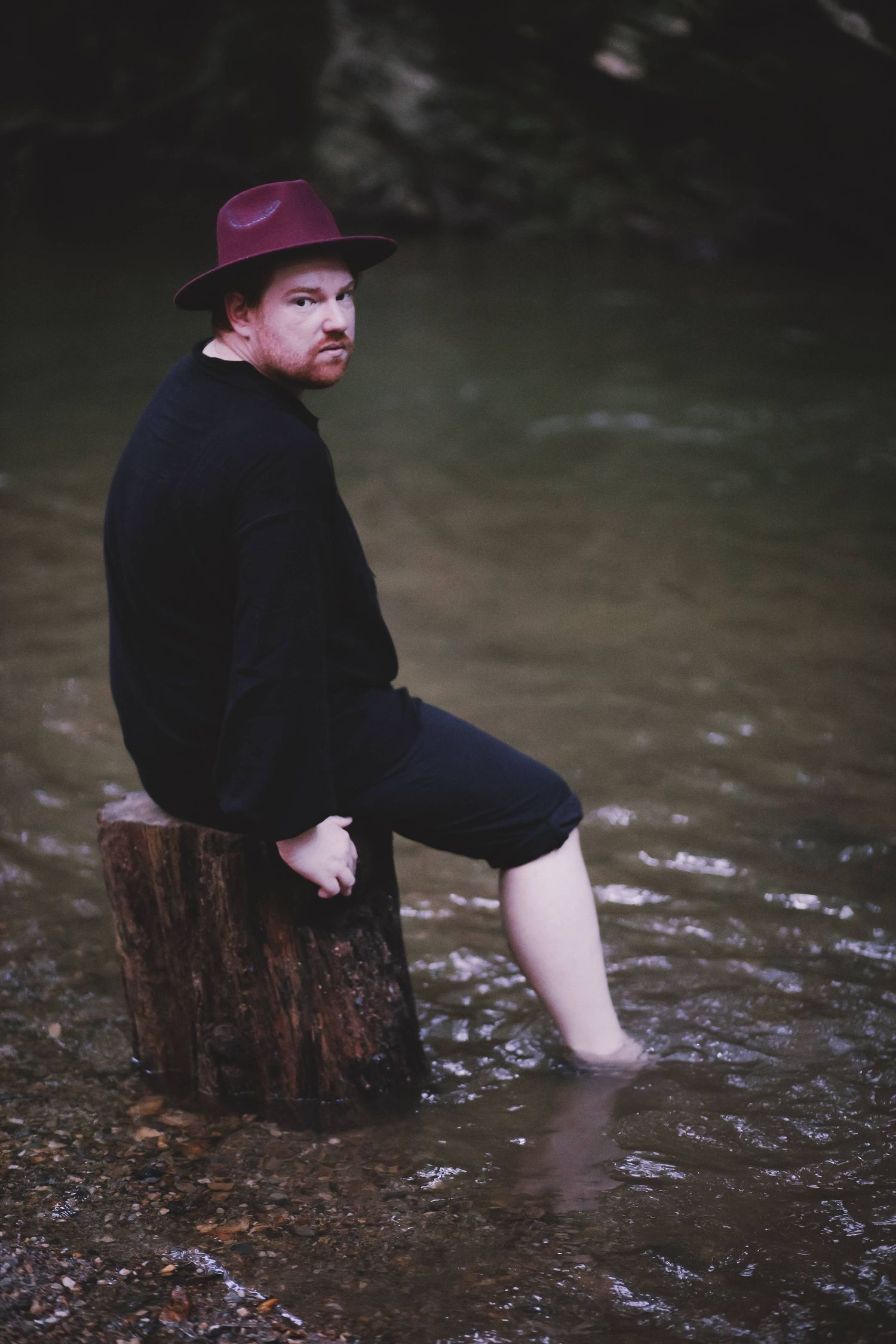 LGBTQ+ inclusive outdoor boudoir session featuring a confident man seated on a creek log in York, Pennsylvania
