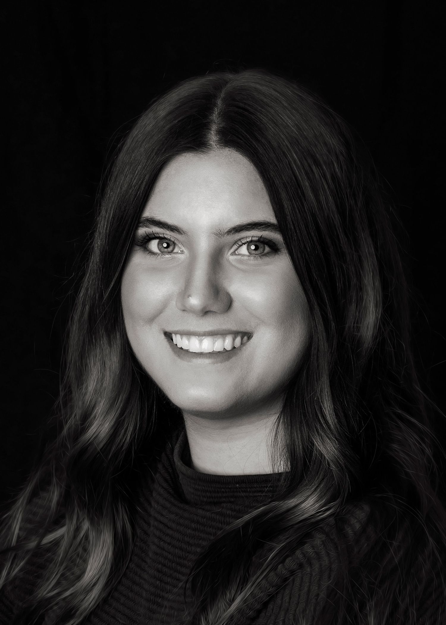 Black and white portrait of a young woman with long dark hair smiling confidently against a dark background.