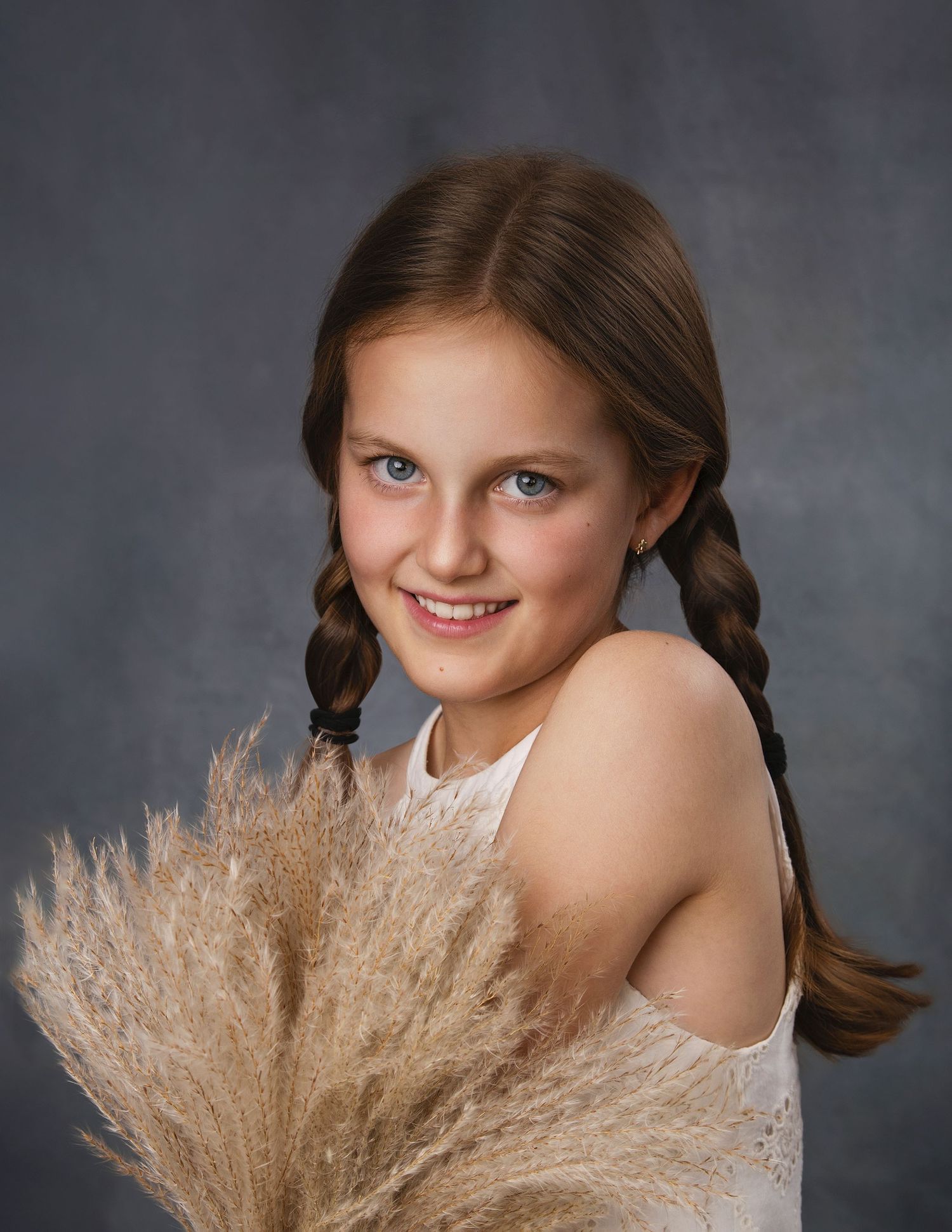 Young girl with braids smiling, holding dried pampas grass in studio portrait photography.