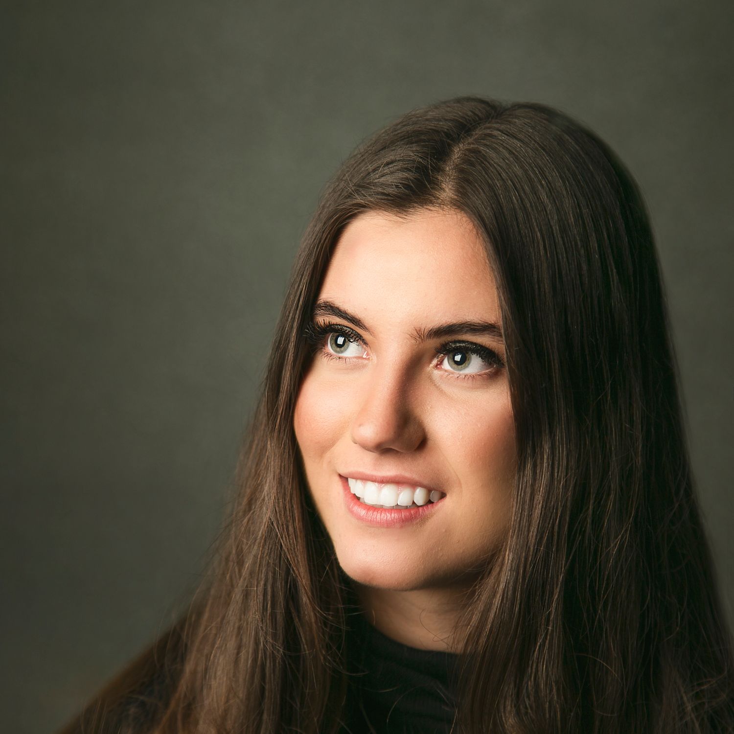 Professional portrait of a smiling young woman with long brown hair against a gray background.
