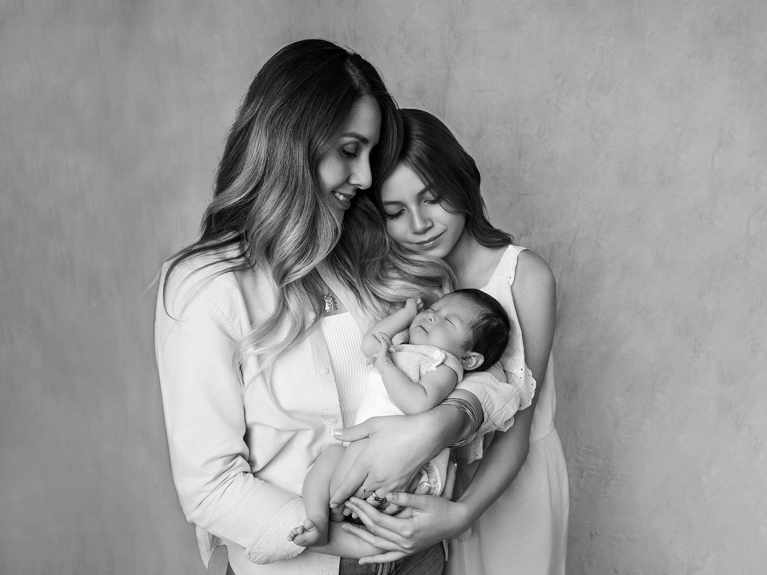 Black and white portrait of two women tenderly holding a sleeping newborn baby.