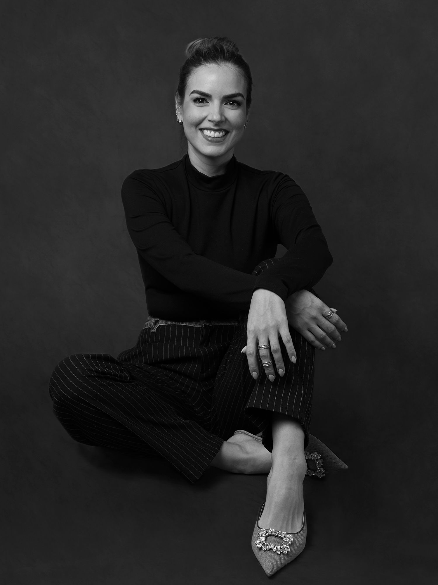 Black and white portrait of woman in black outfit seated on floor with crossed legs.