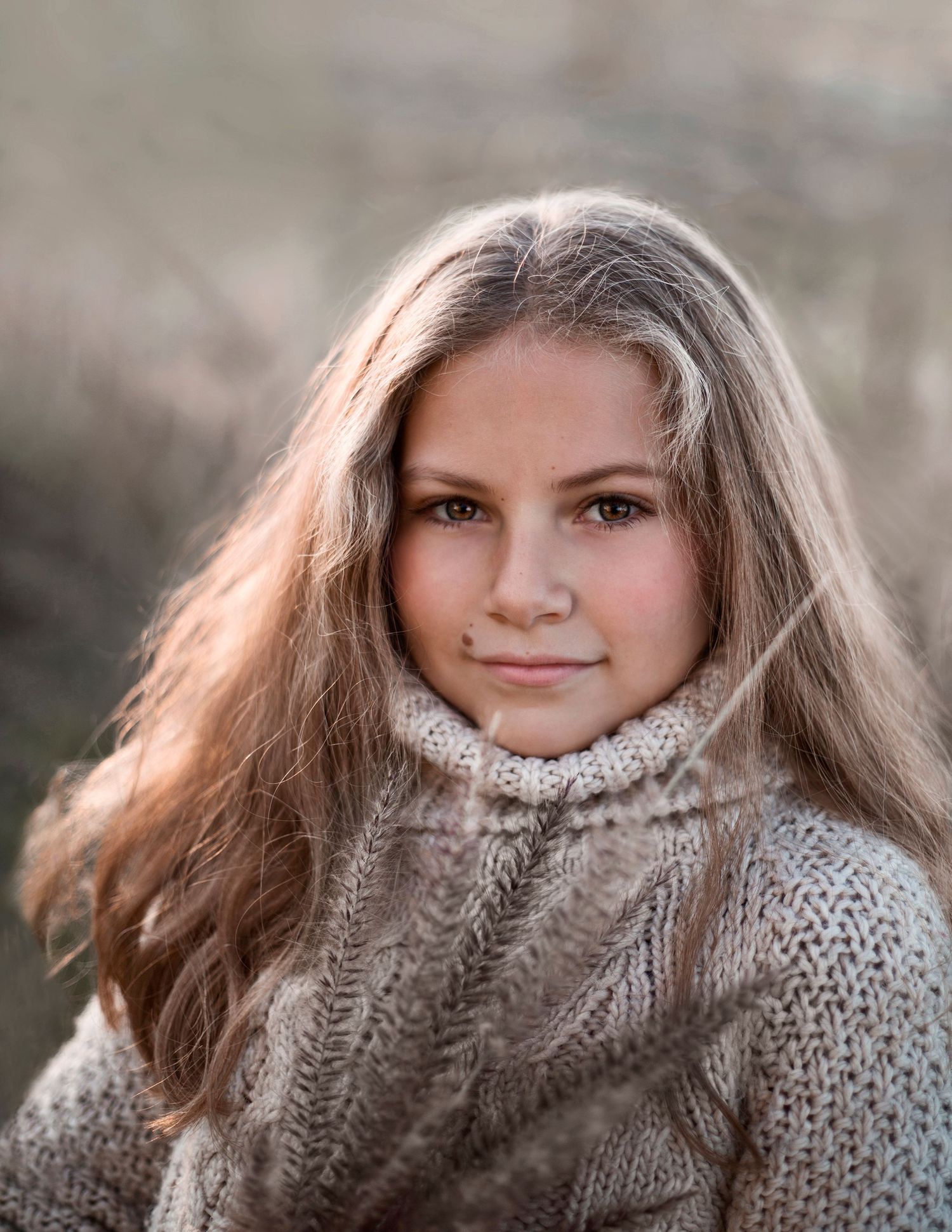 Portrait of teenage girl with long blonde hair wearing cozy knit sweater in autumn outdoor setting.