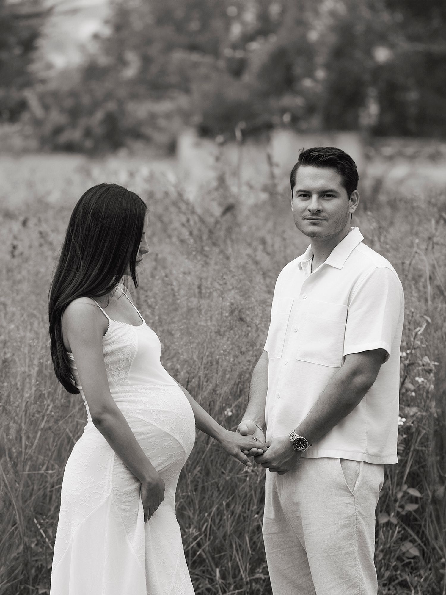 Black and white photo of pregnant couple holding hands in a field.