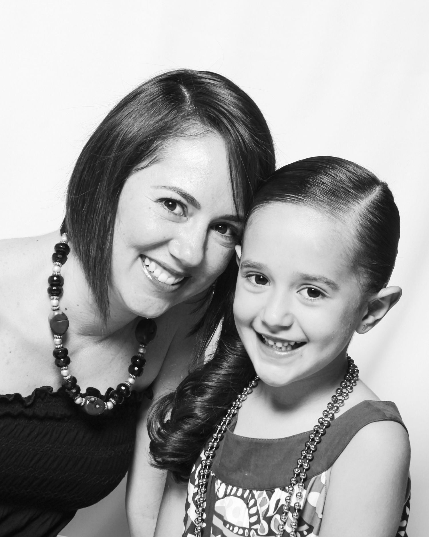 Black and white studio portrait of a smiling mother and young daughter wearing beaded necklaces.
