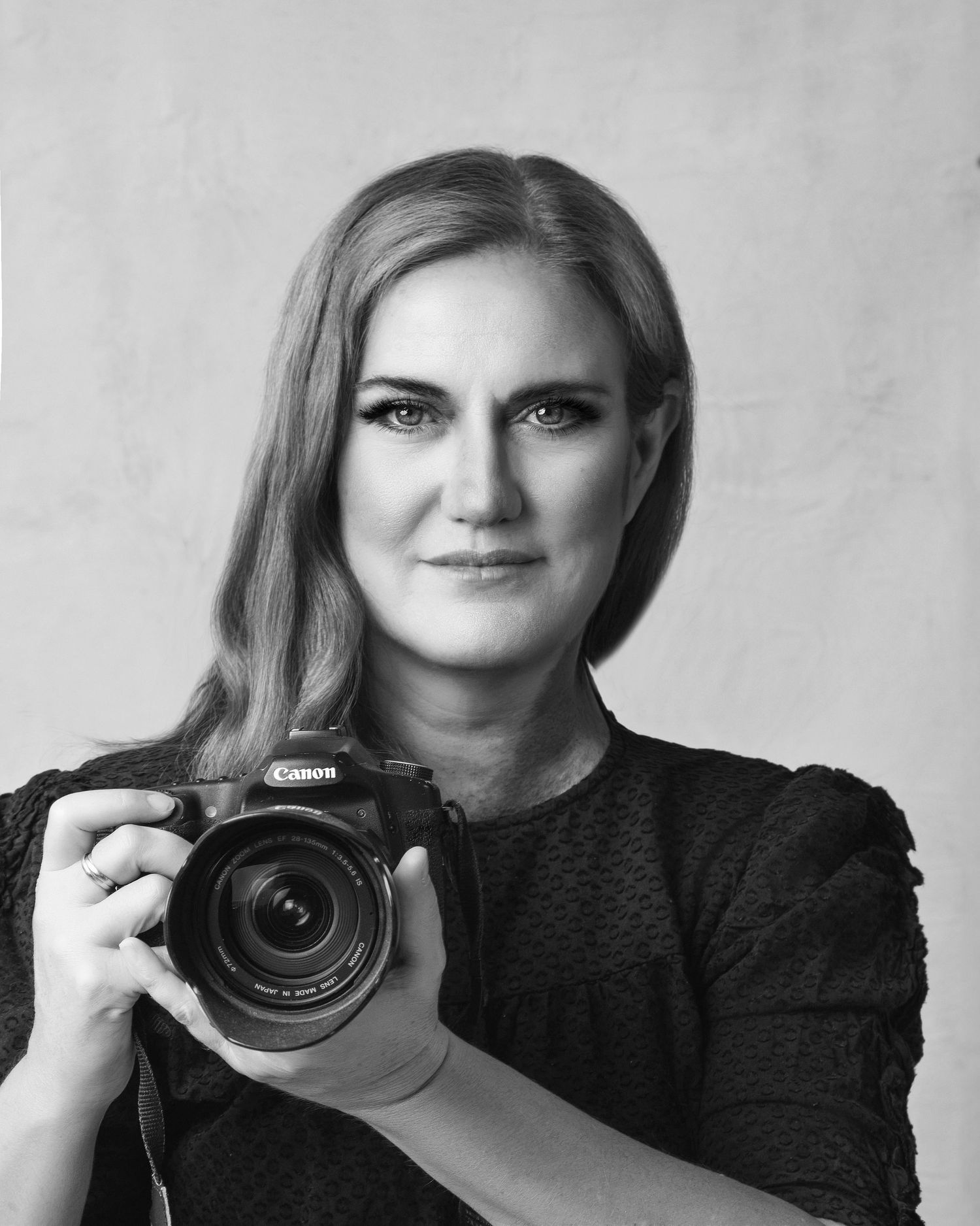 Black and white portrait of a female photographer holding a Canon camera in a studio.
