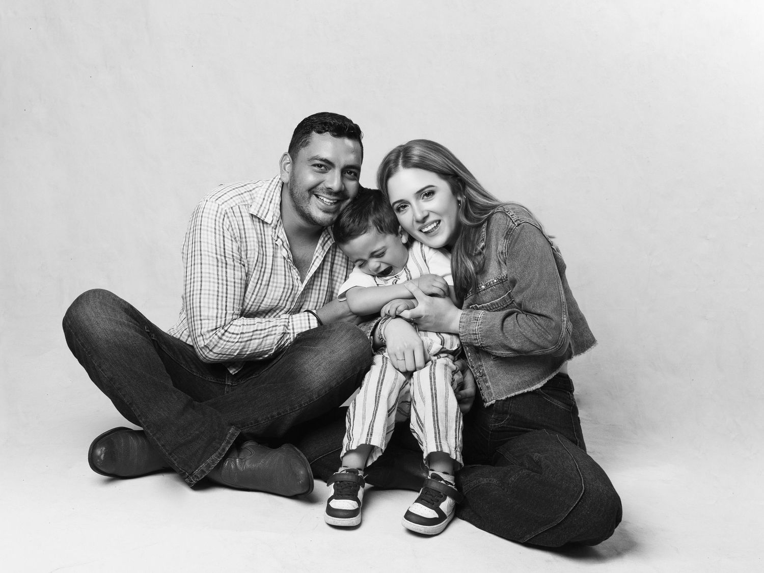 Black and white studio portrait of a happy family of three sitting on the floor.