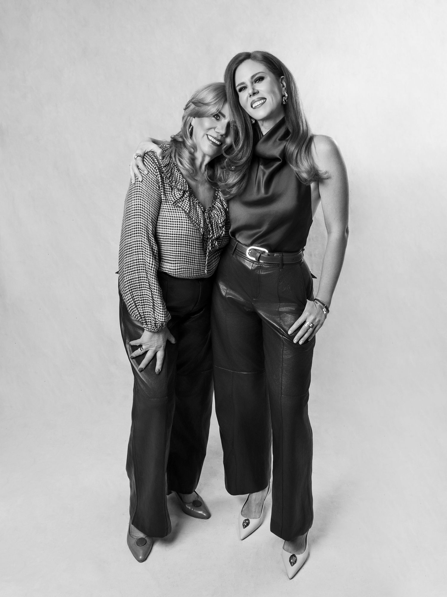 Black and white portrait of two elegantly dressed women posing together, smiling in a studio setting.