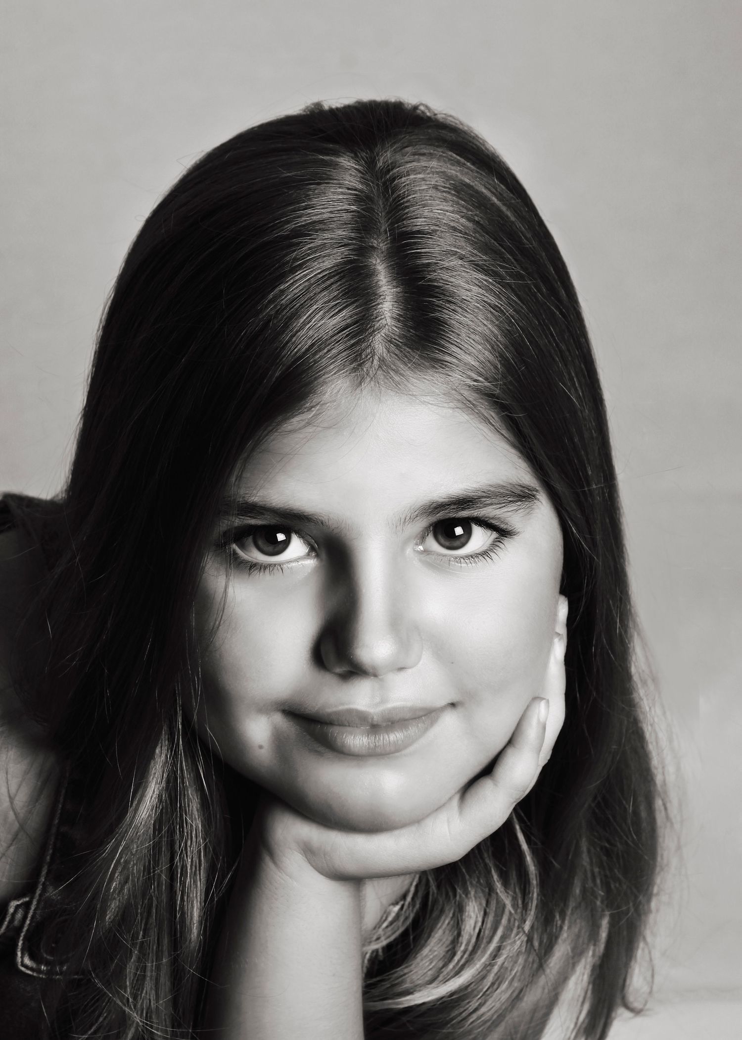 Black and white portrait of a young girl with dark hair resting chin on hand.
