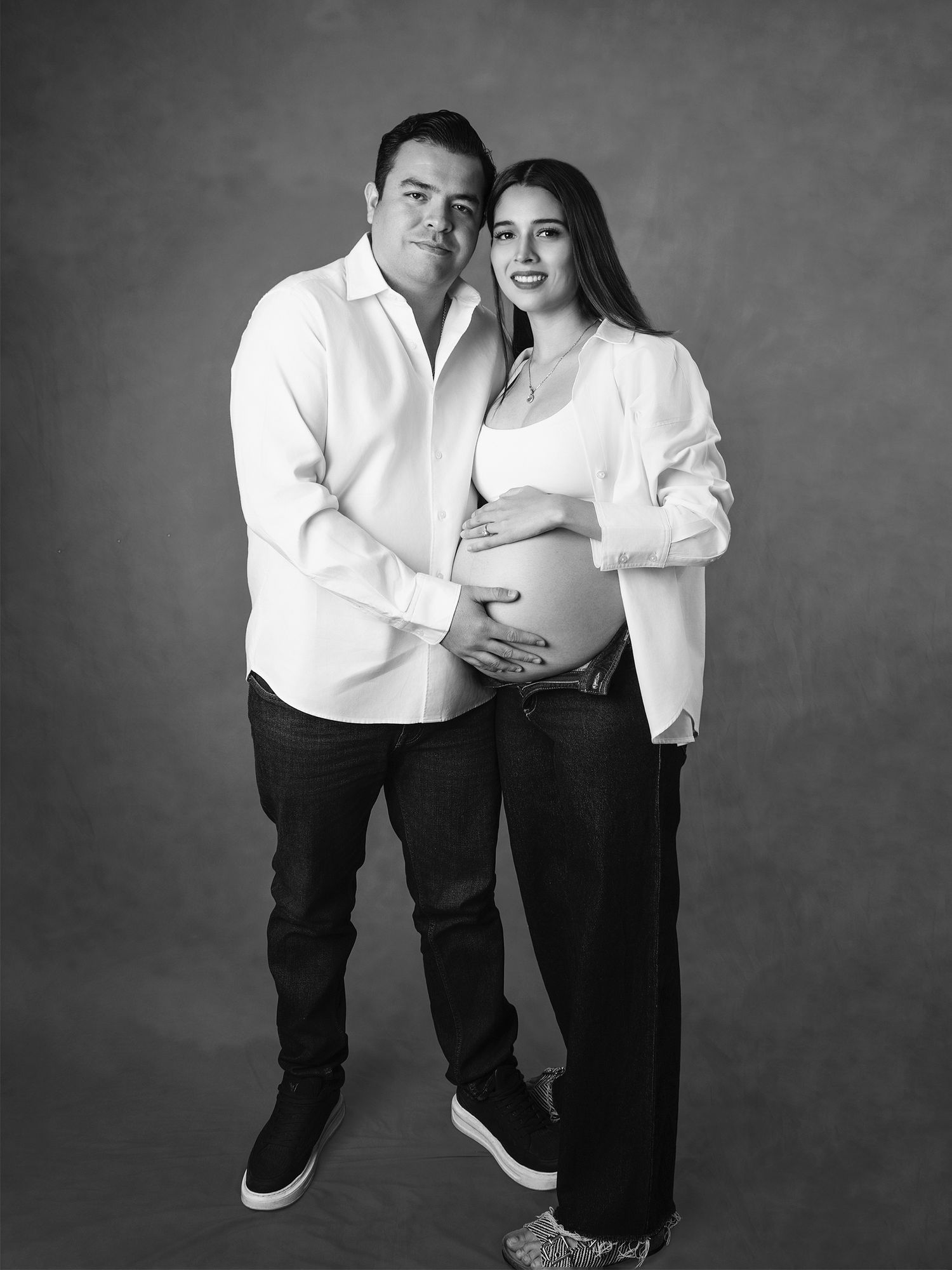 Black and white studio portrait of couple with pregnant woman showing bump.
