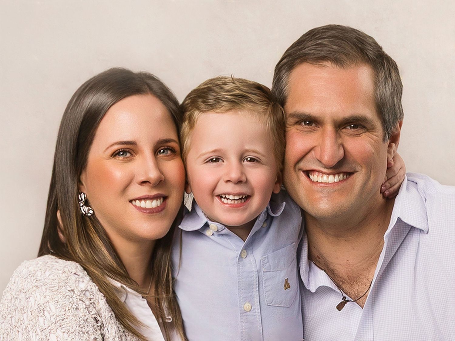 Smiling family of three with young boy between parents in warm studio portrait.