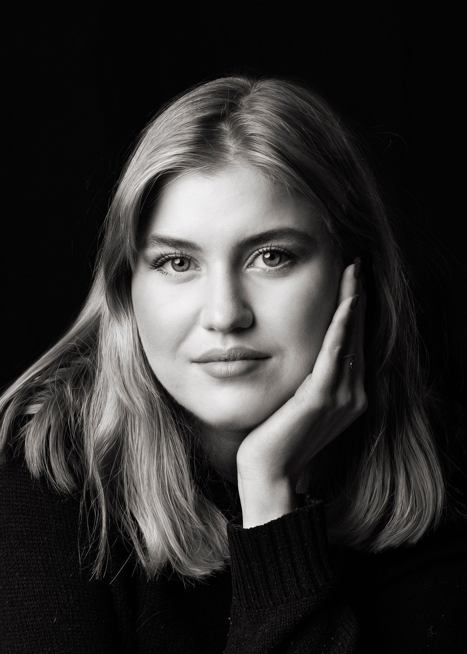 Black and white close-up portrait of young blonde woman resting chin on hand.
