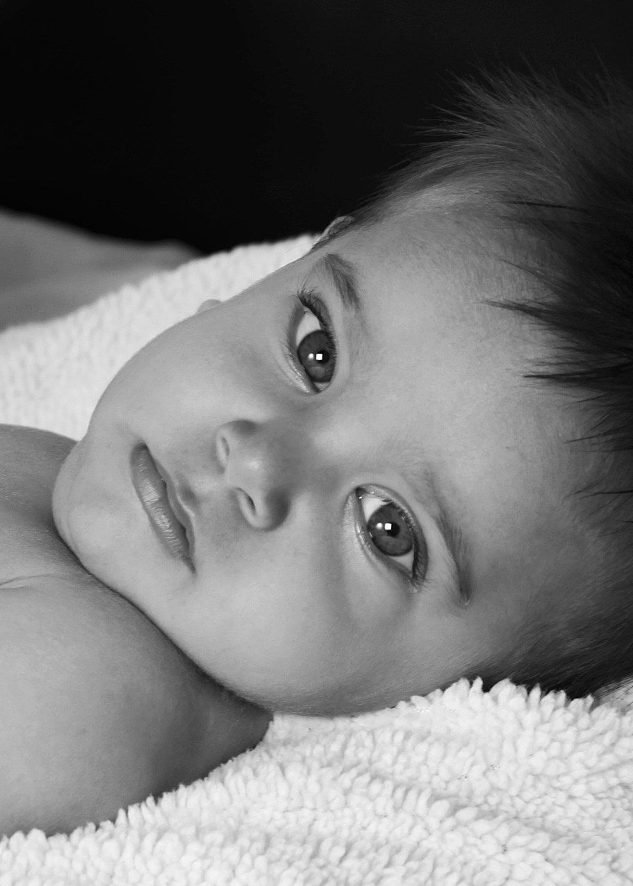 Close-up black and white portrait of a newborn baby with big expressive eyes on a blanket.