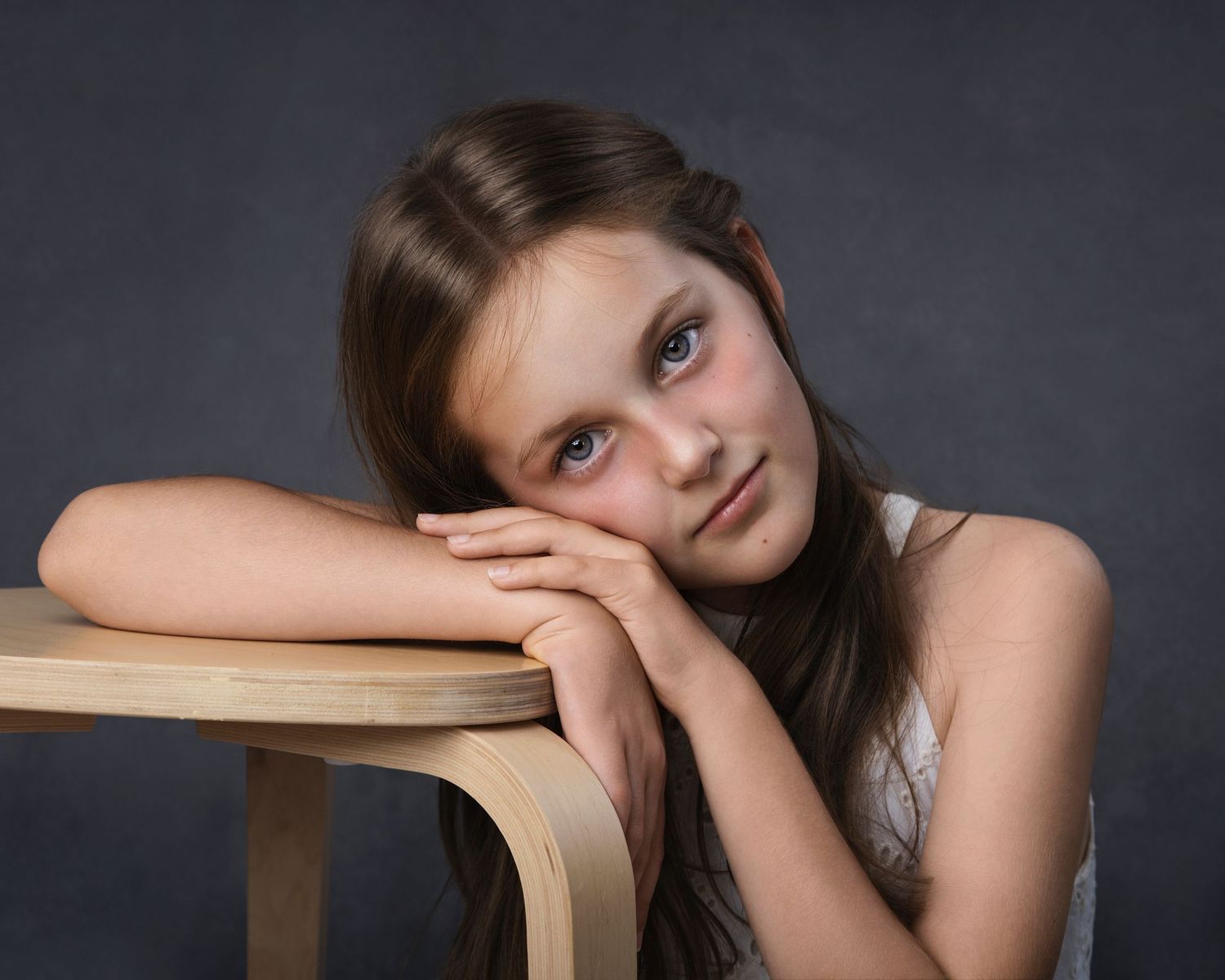 Portrait of a young brunette girl leaning on a wooden chair with a thoughtful expression.