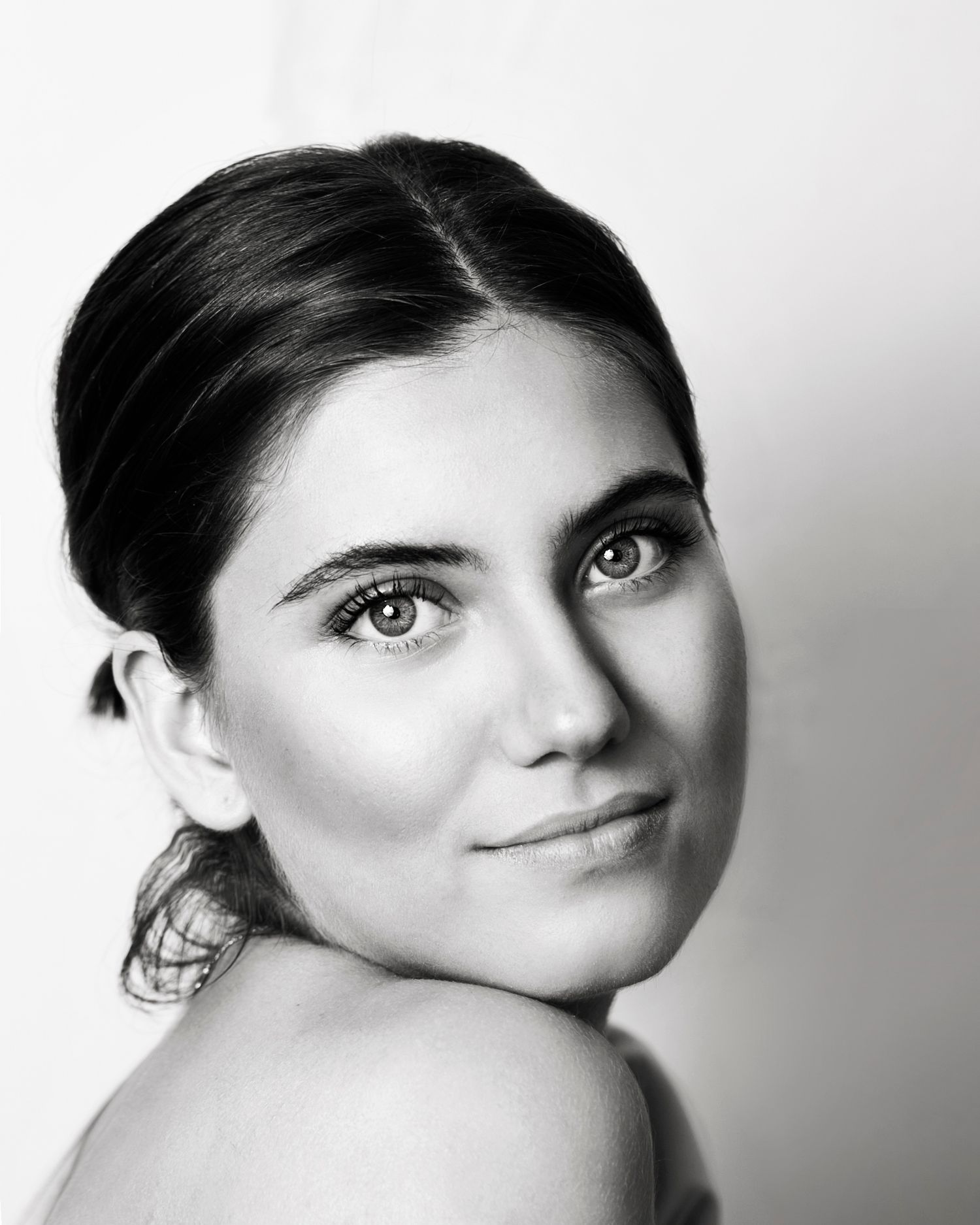 Elegant black and white portrait of a young brunette woman with hair up looking over her bare shoulder.