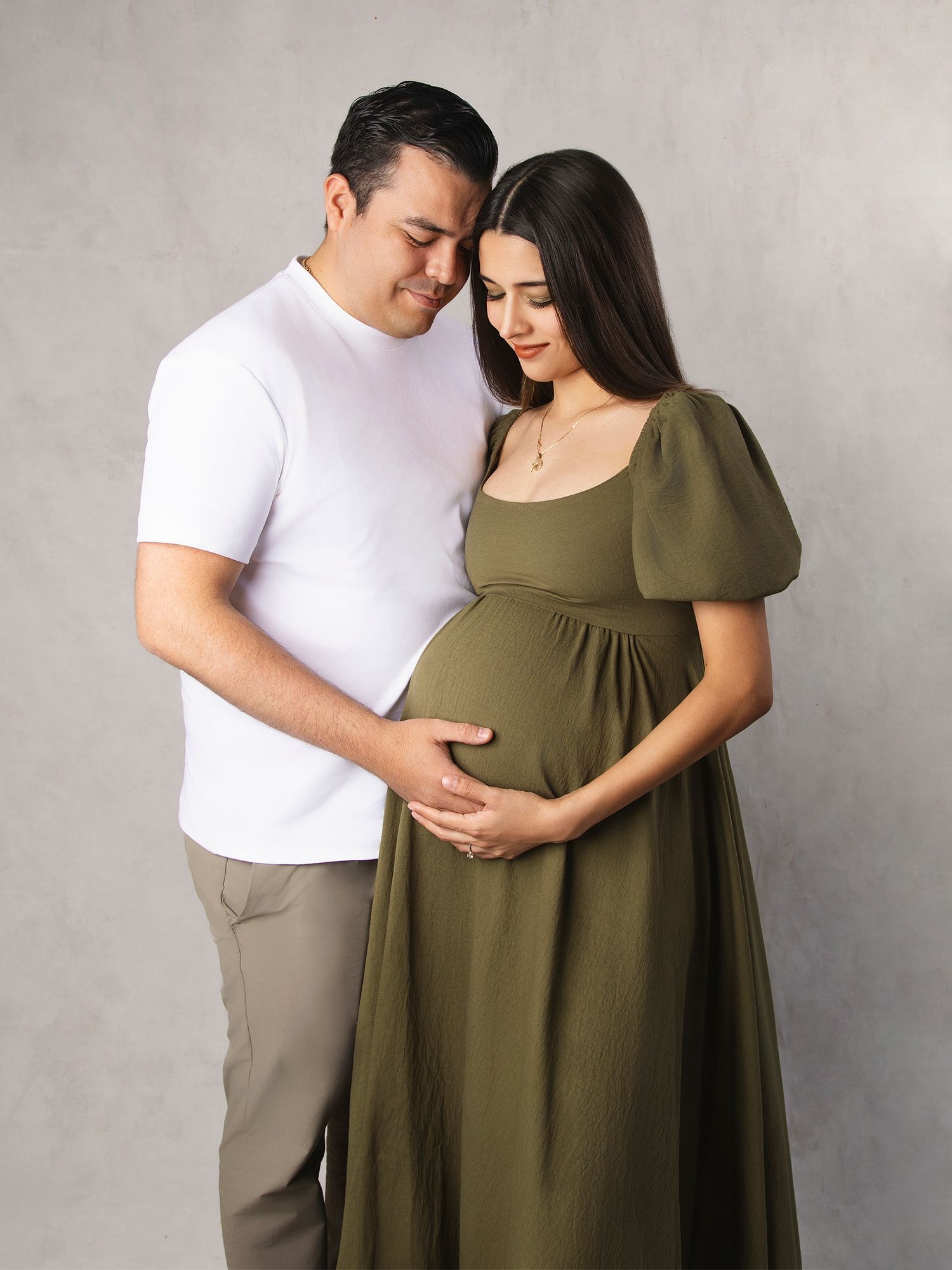 Couple in studio tenderly cradling pregnant belly in olive dress.