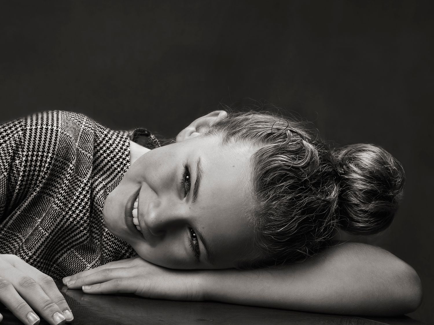 Black and white photo of a smiling young girl with a bun hairstyle resting on a surface.