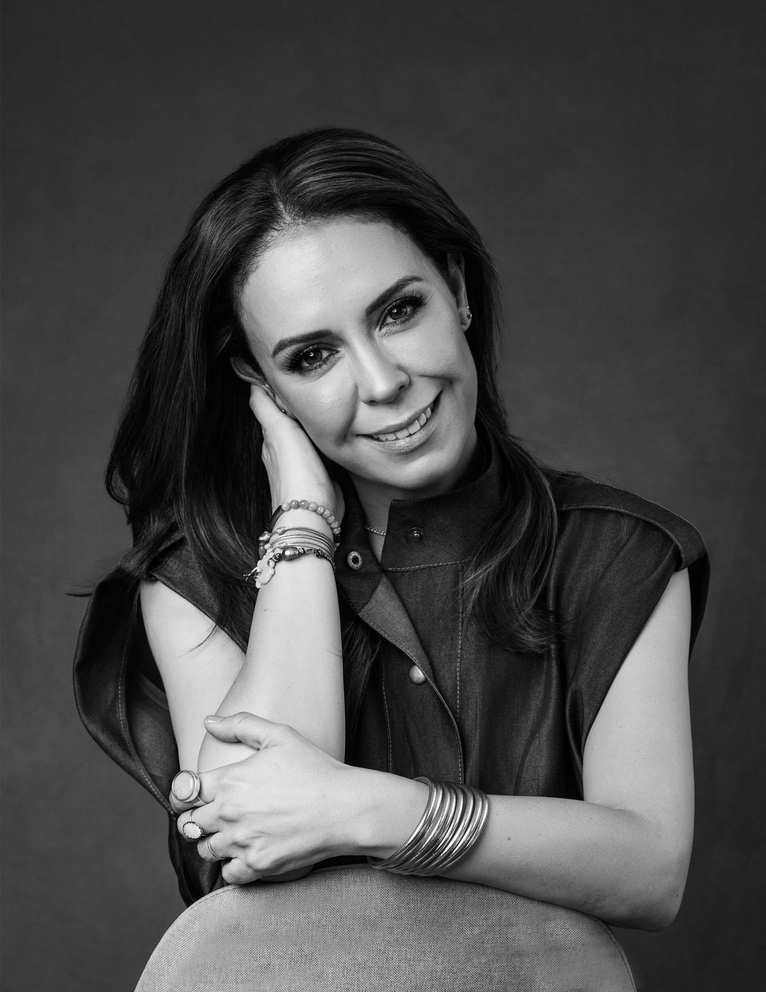 Black and white close-up portrait of smiling woman with bracelets resting chin on hand.