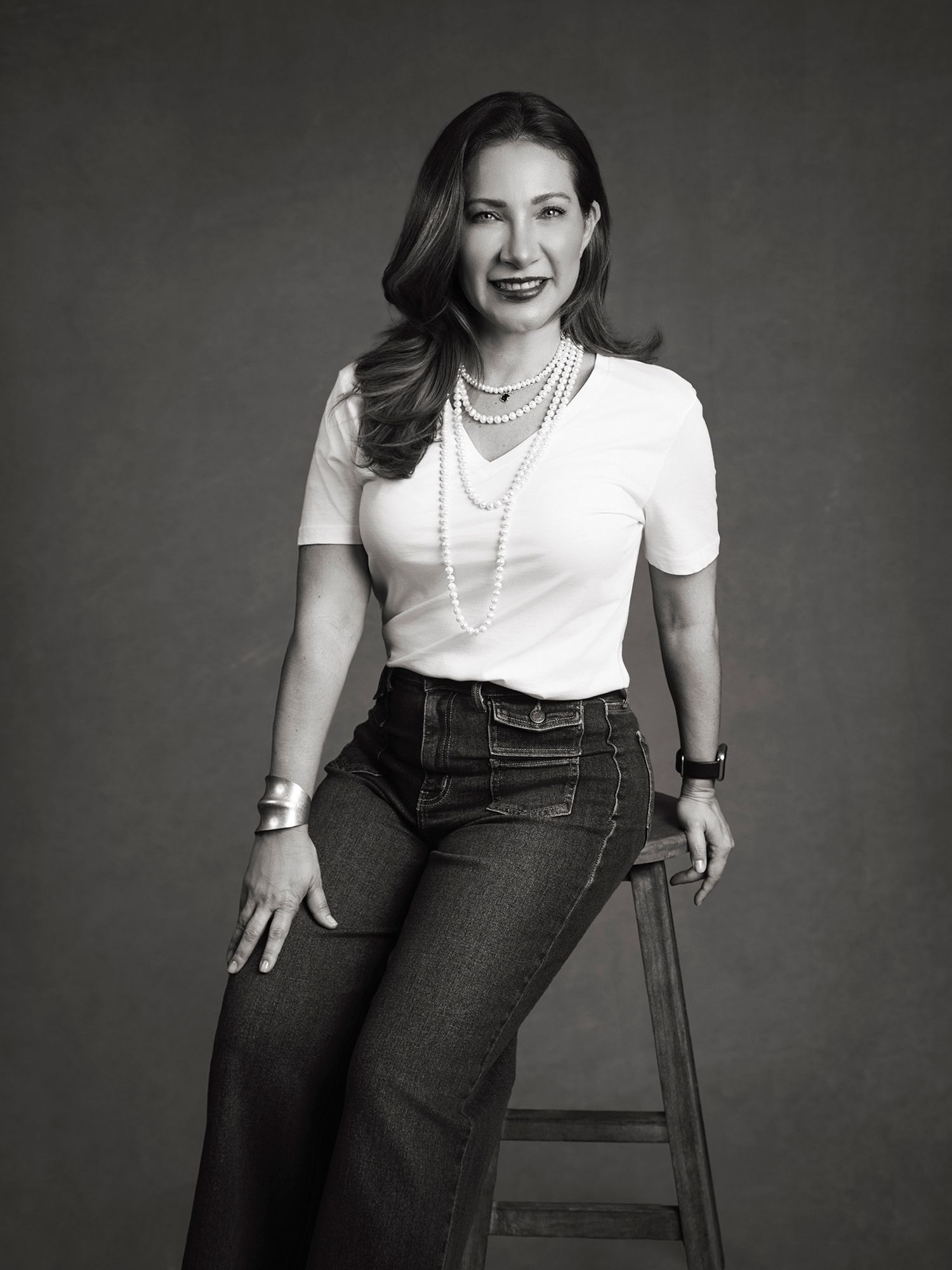 Black and white portrait of woman in white tee and jeans with layered pearl necklaces.