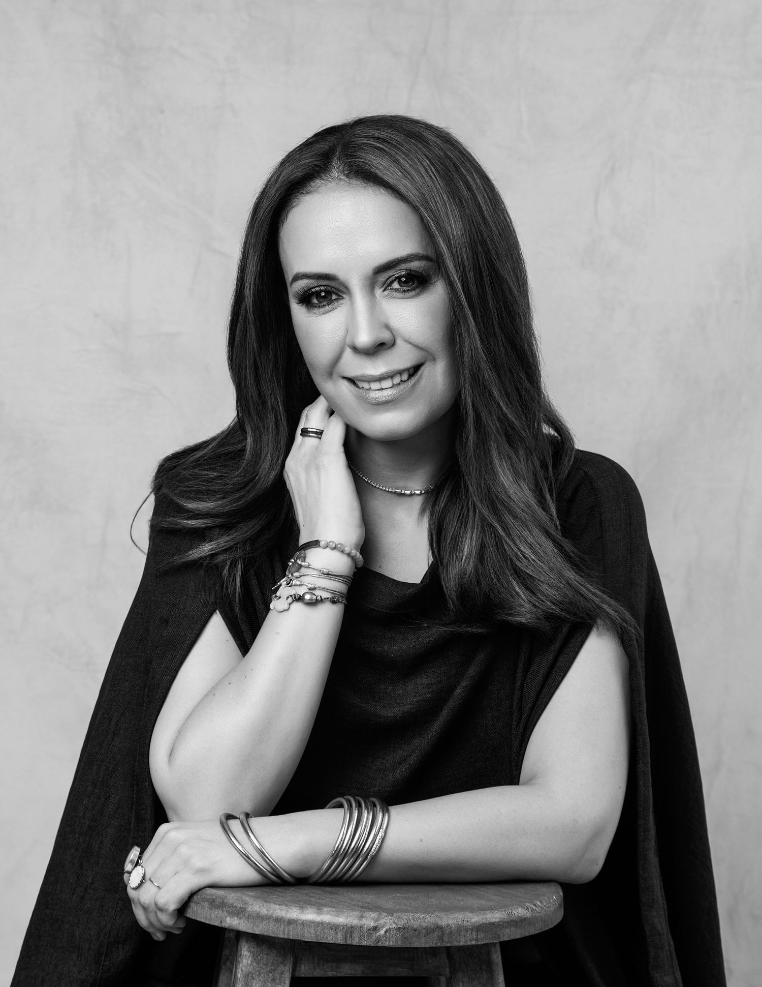 Black and white studio portrait of woman in black cape top with layered bracelets.