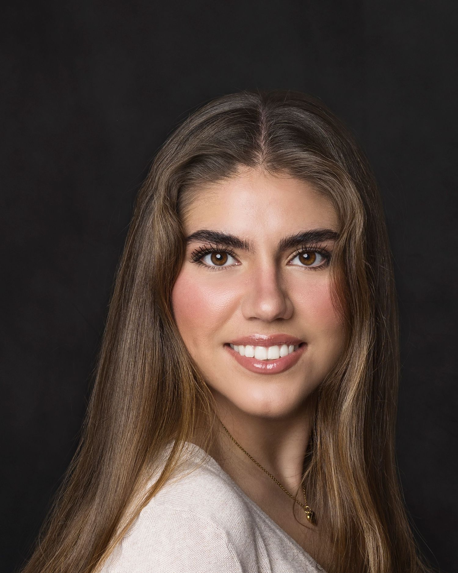 Smiling young woman with long brown hair posing for a portrait against a dark background.