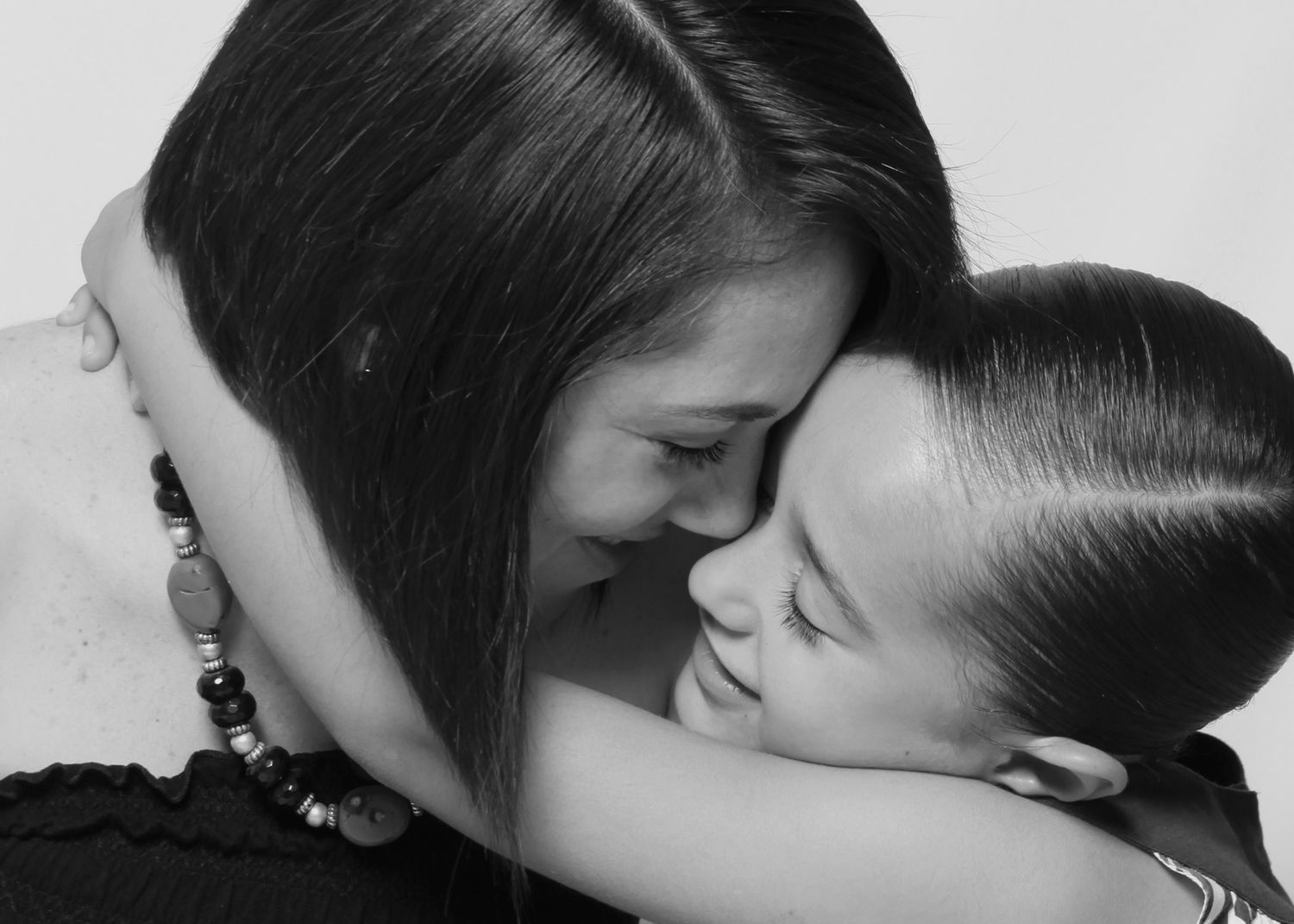 Black and white close-up portrait of a mother and daughter sharing a tender embrace.