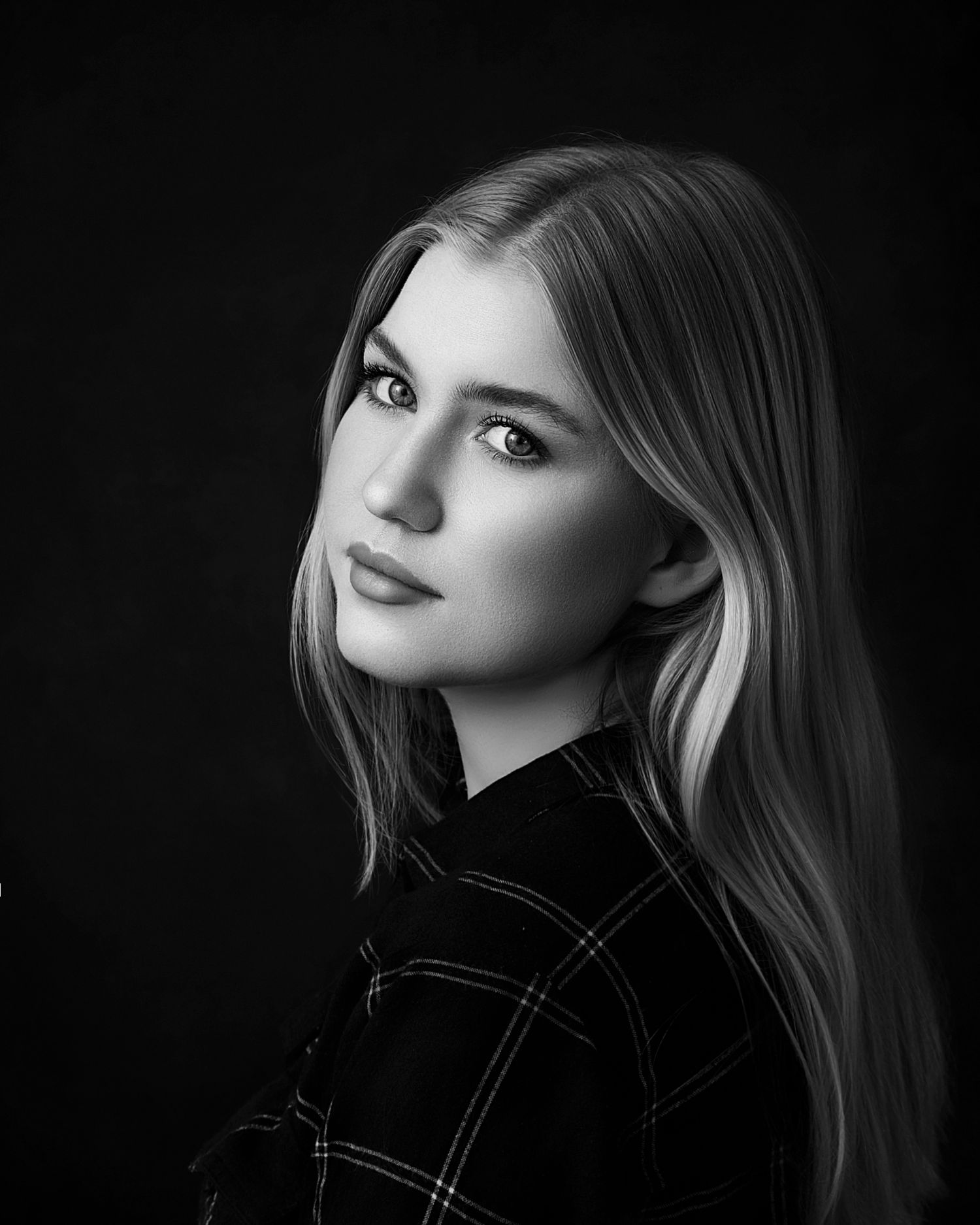 Black and white portrait of a young blonde woman in a plaid jacket gazing over her shoulder.