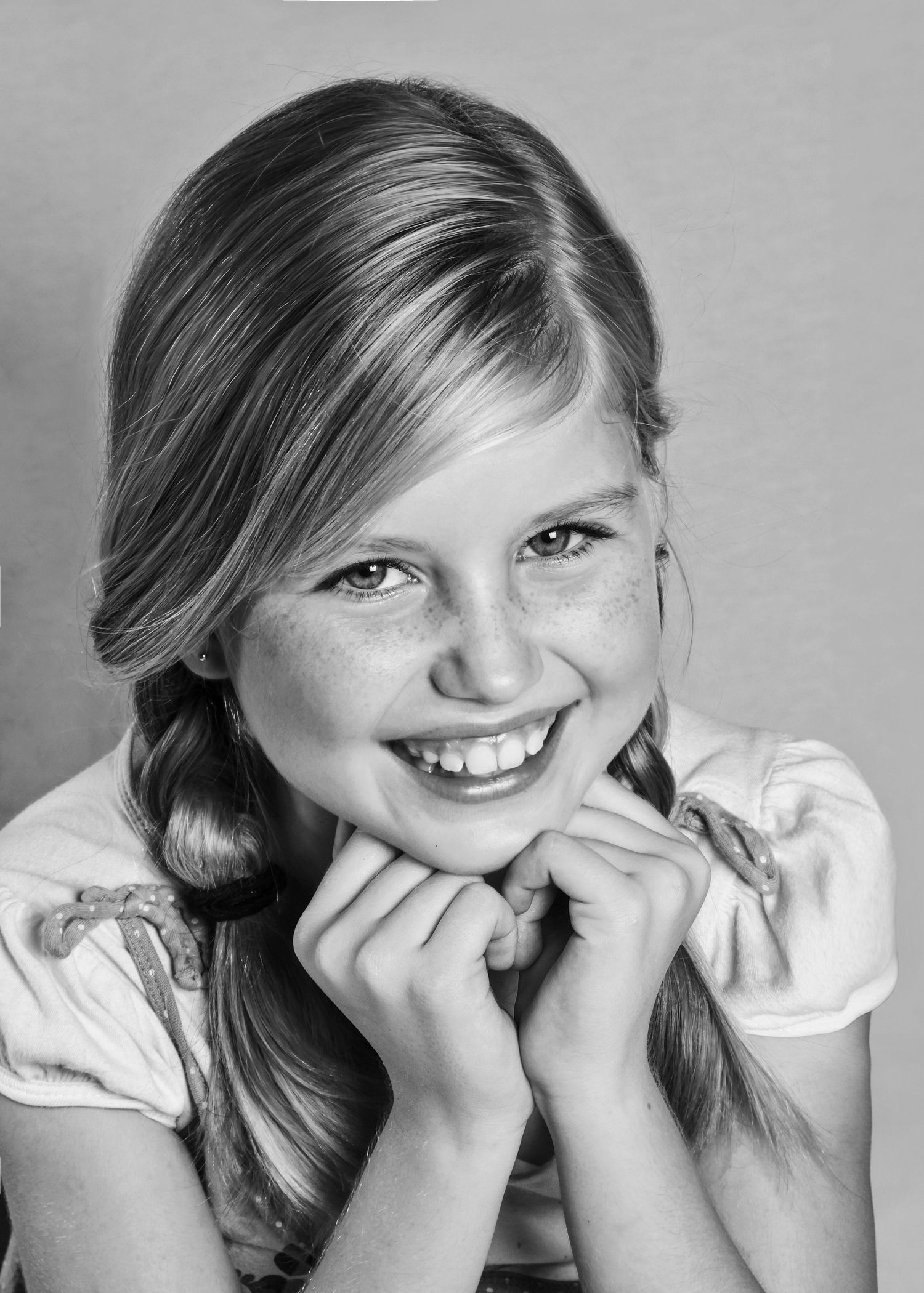 Black and white portrait of a smiling freckled girl with blonde braids and bright smile.