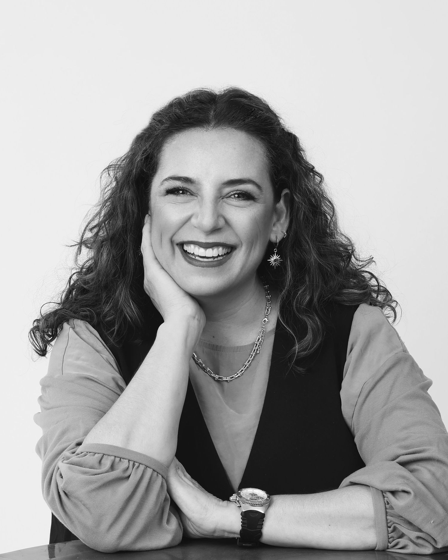 Black and white portrait of a curly-haired woman smiling warmly with hand resting on her cheek.