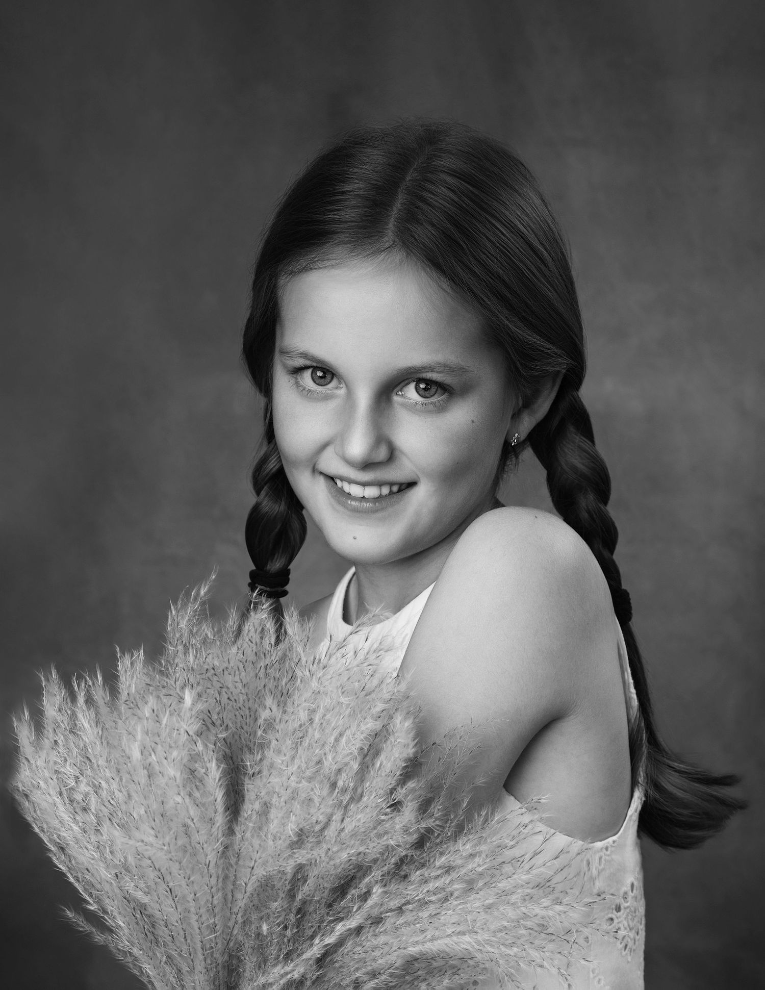 Black and white portrait of a smiling girl with braids holding dried pampas grass.