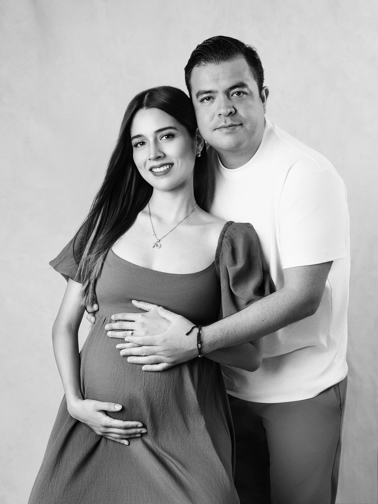 Black and white studio portrait of smiling pregnant couple embracing.