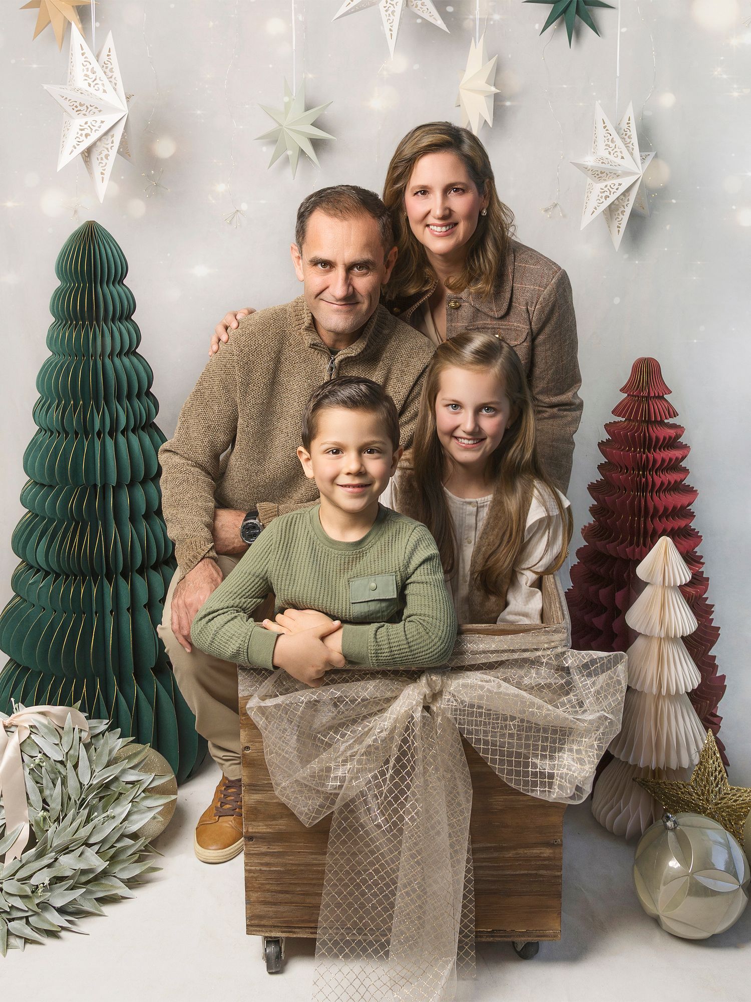 Family Christmas portrait with parents and two children surrounded by festive holiday decorations.