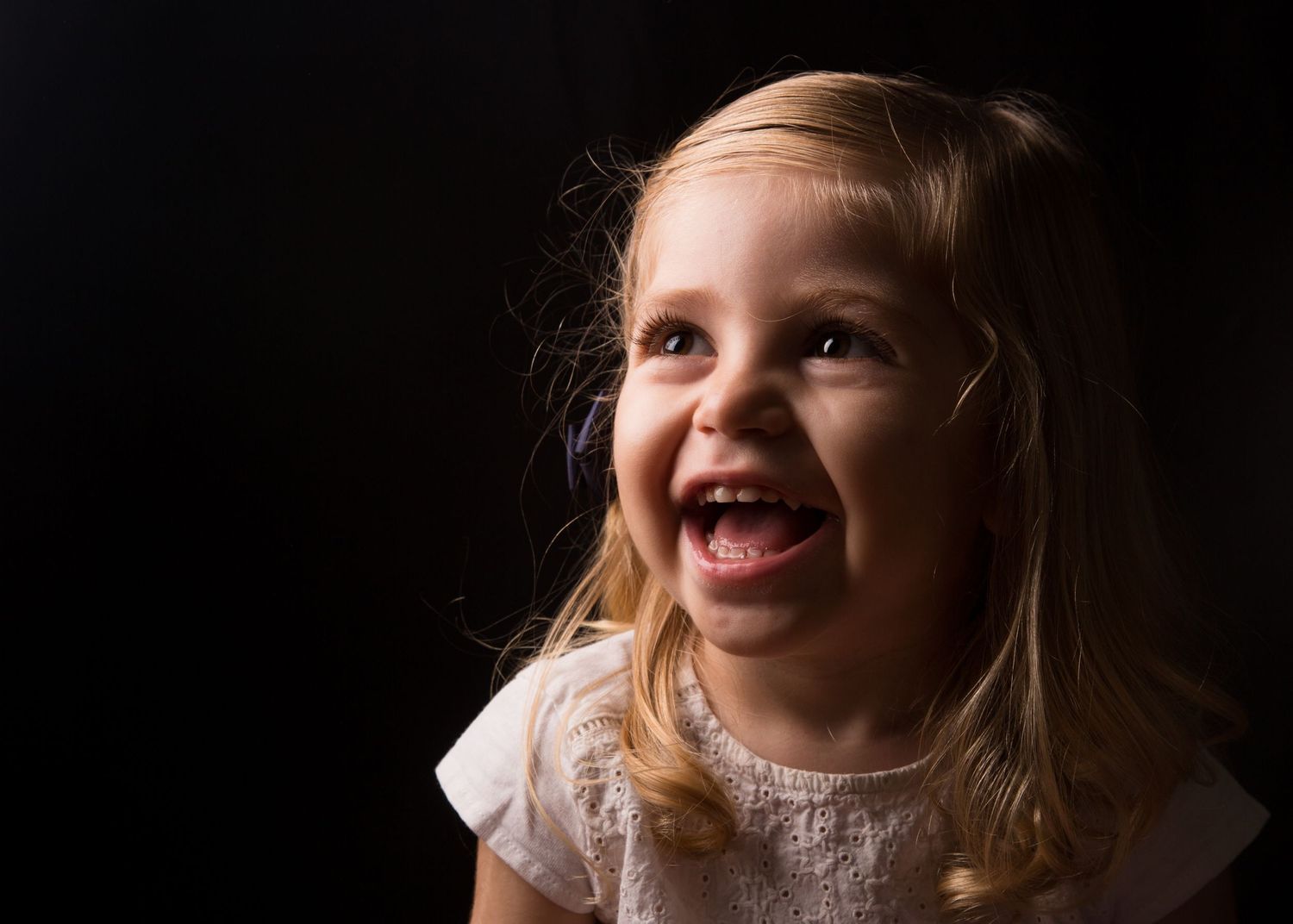 Laughing blonde girl with joyful expression against dark background in studio portrait.