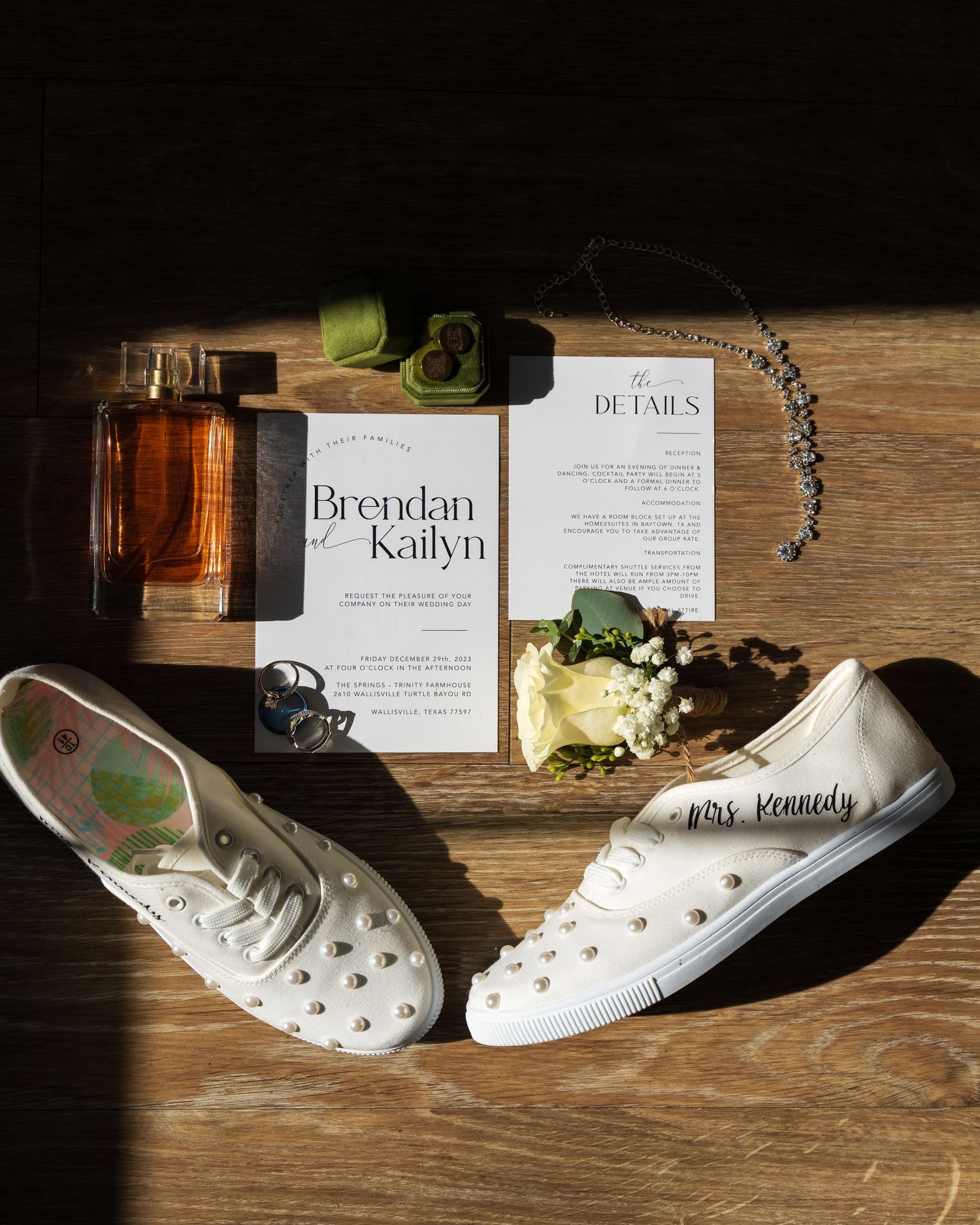 Wedding details flatlay with invitation, white sneakers, champagne and floral accents on wooden surface.