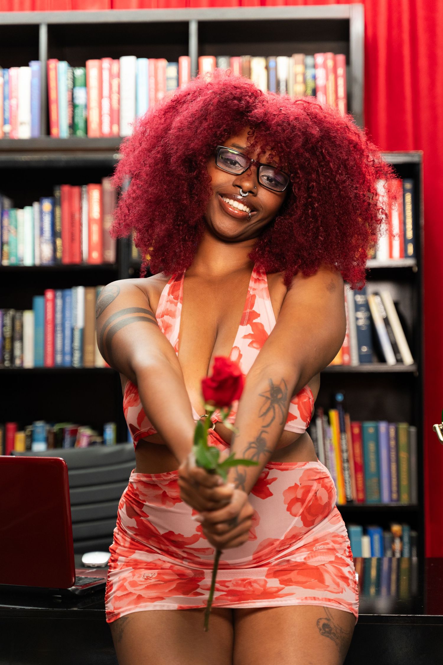 Boudoir library photoshoot with red curtains and bookshelves in background.