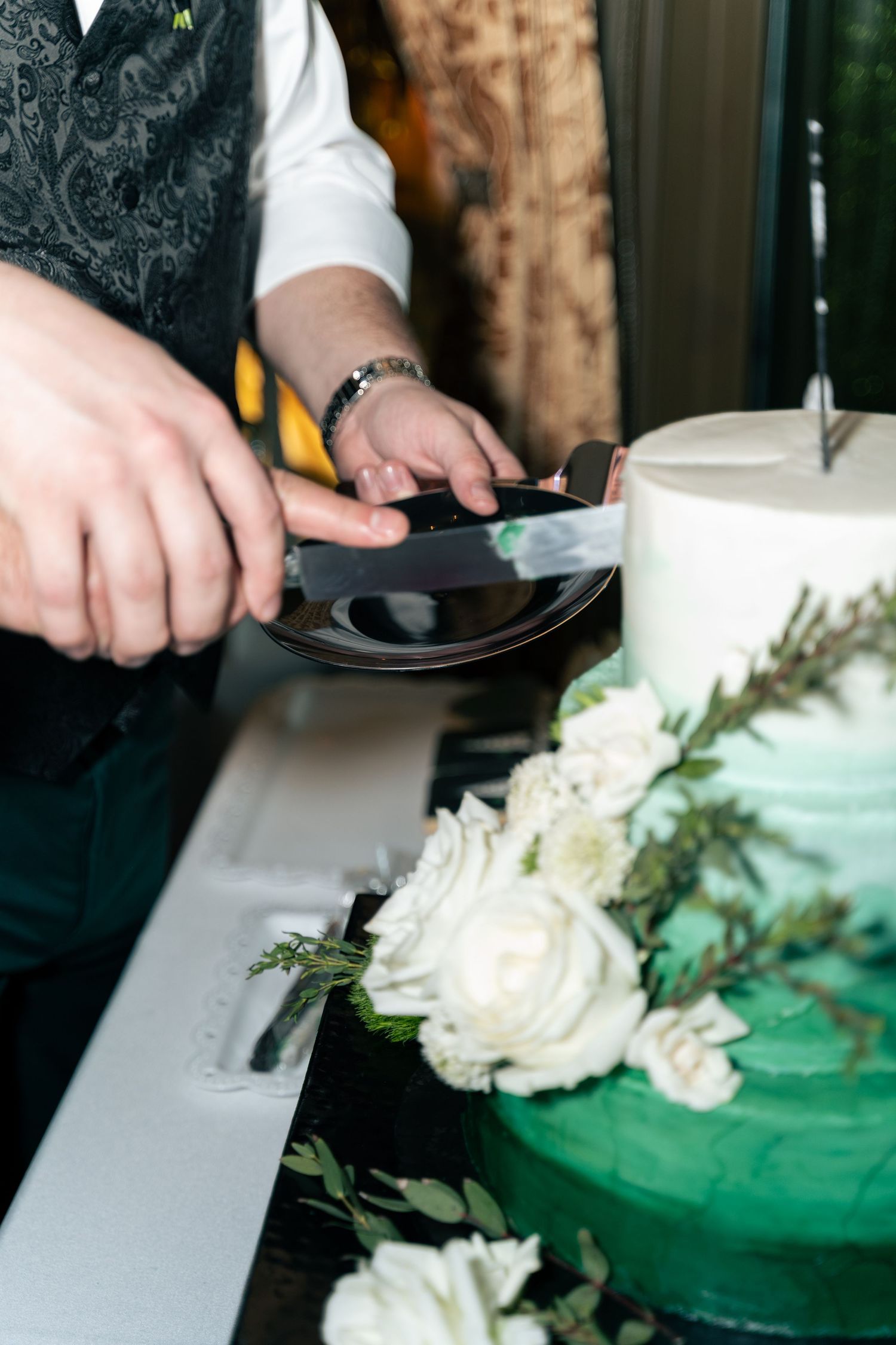 Hands cutting into a white and green ombre wedding cake with floral decorations.