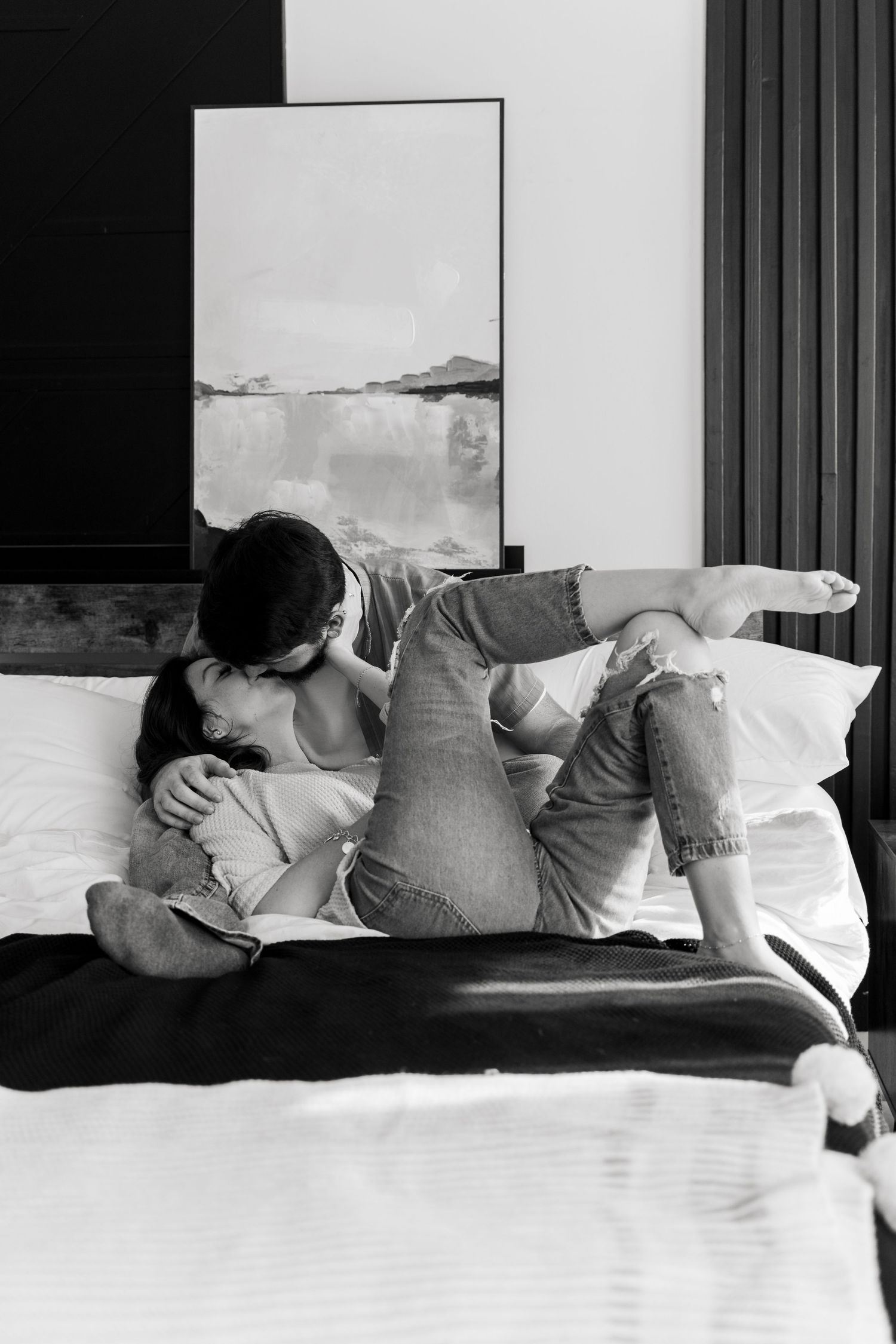 A black and white photo of a romantic couple embracing and kissing on a white bed.