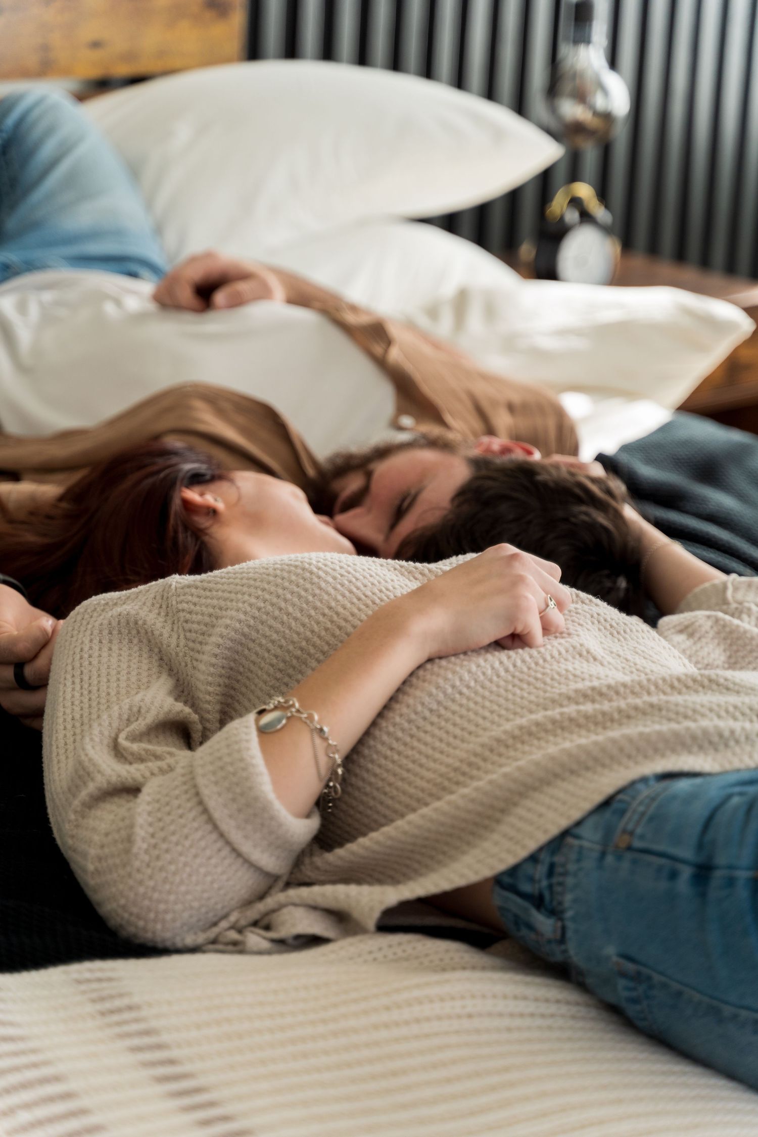 Couple lying together on a bed with white pillows, sharing an intimate moment in casual cozy clothing.