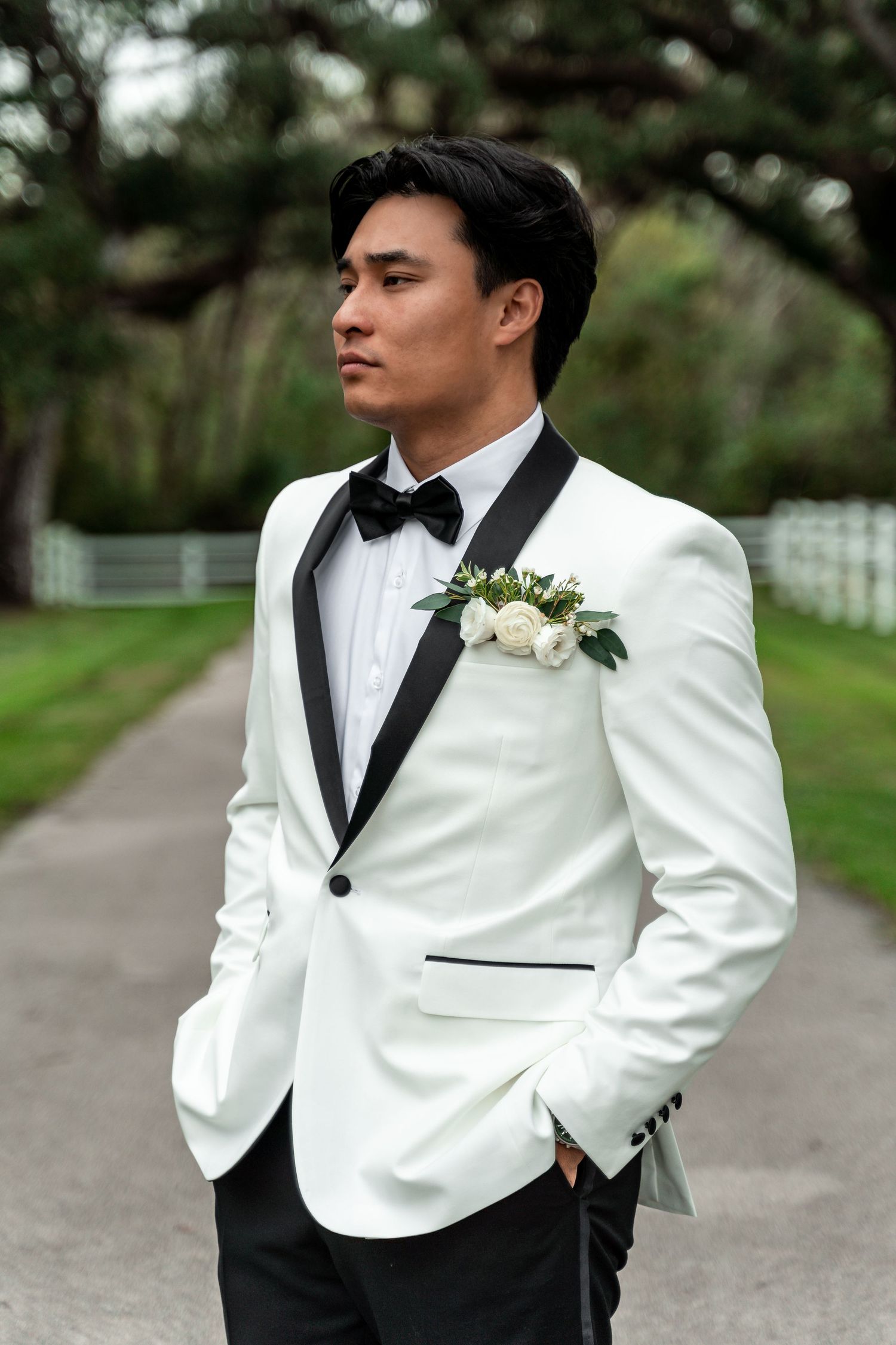 Groom in white tuxedo jacket poses for stylish wedding portraits outdoors.