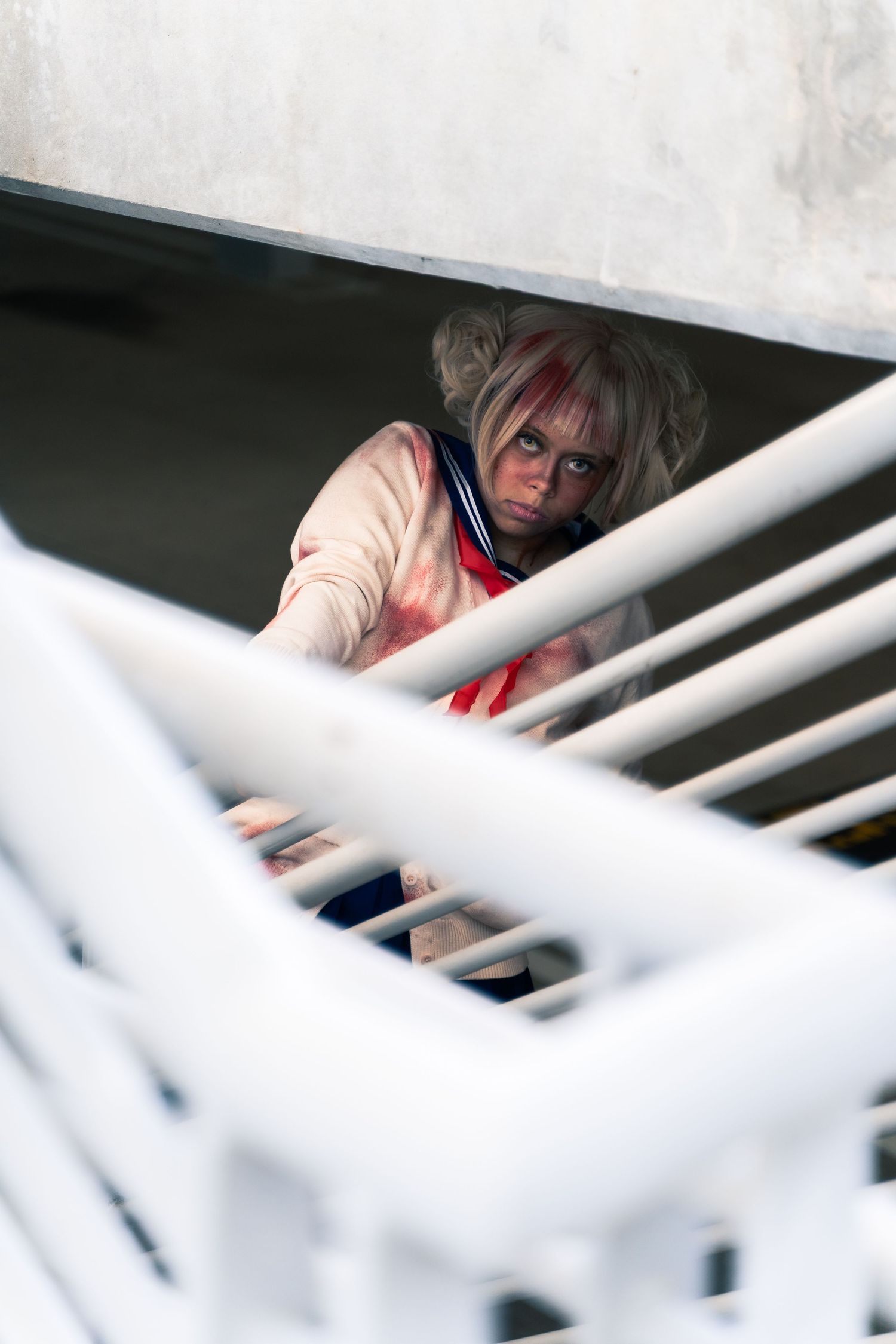 Figure seen through white railings wearing light colored clothing and red accents in a dimly lit space.