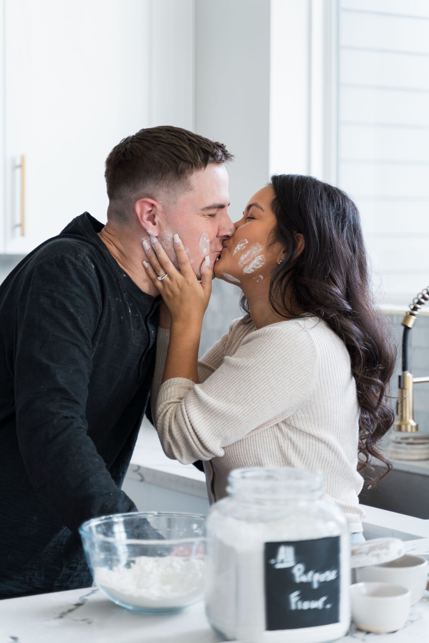 A couple shares a playful kiss in the kitchen, faces dusted with flour while baking together.