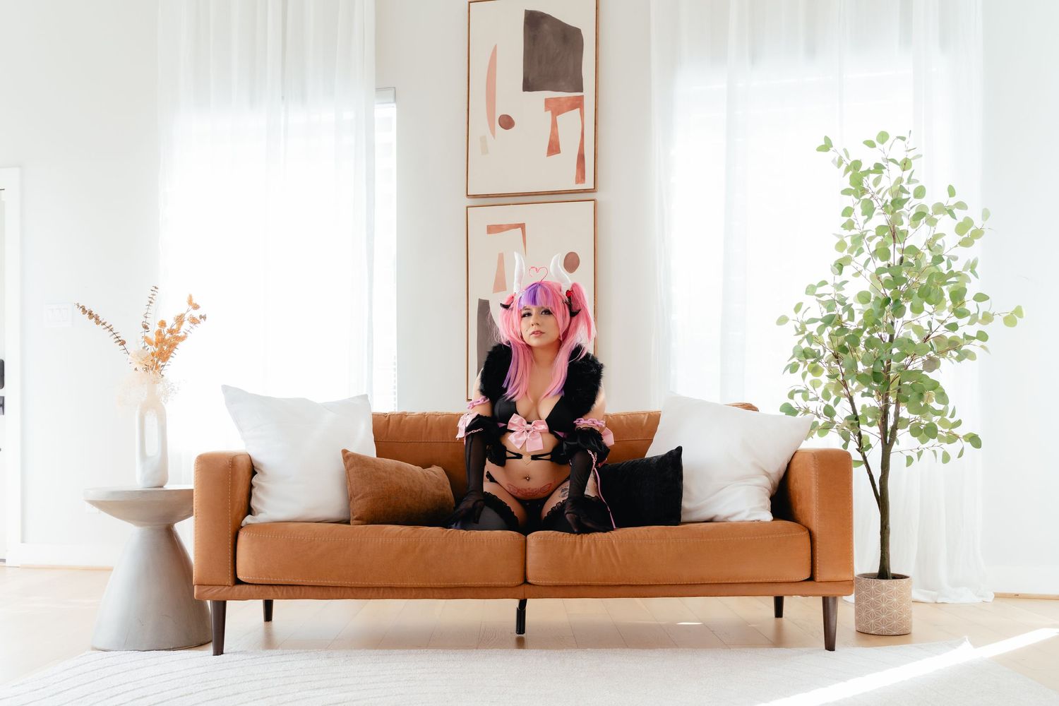Person with pink hair in black outfit sitting on brown leather sofa in bright modern living room with plants.